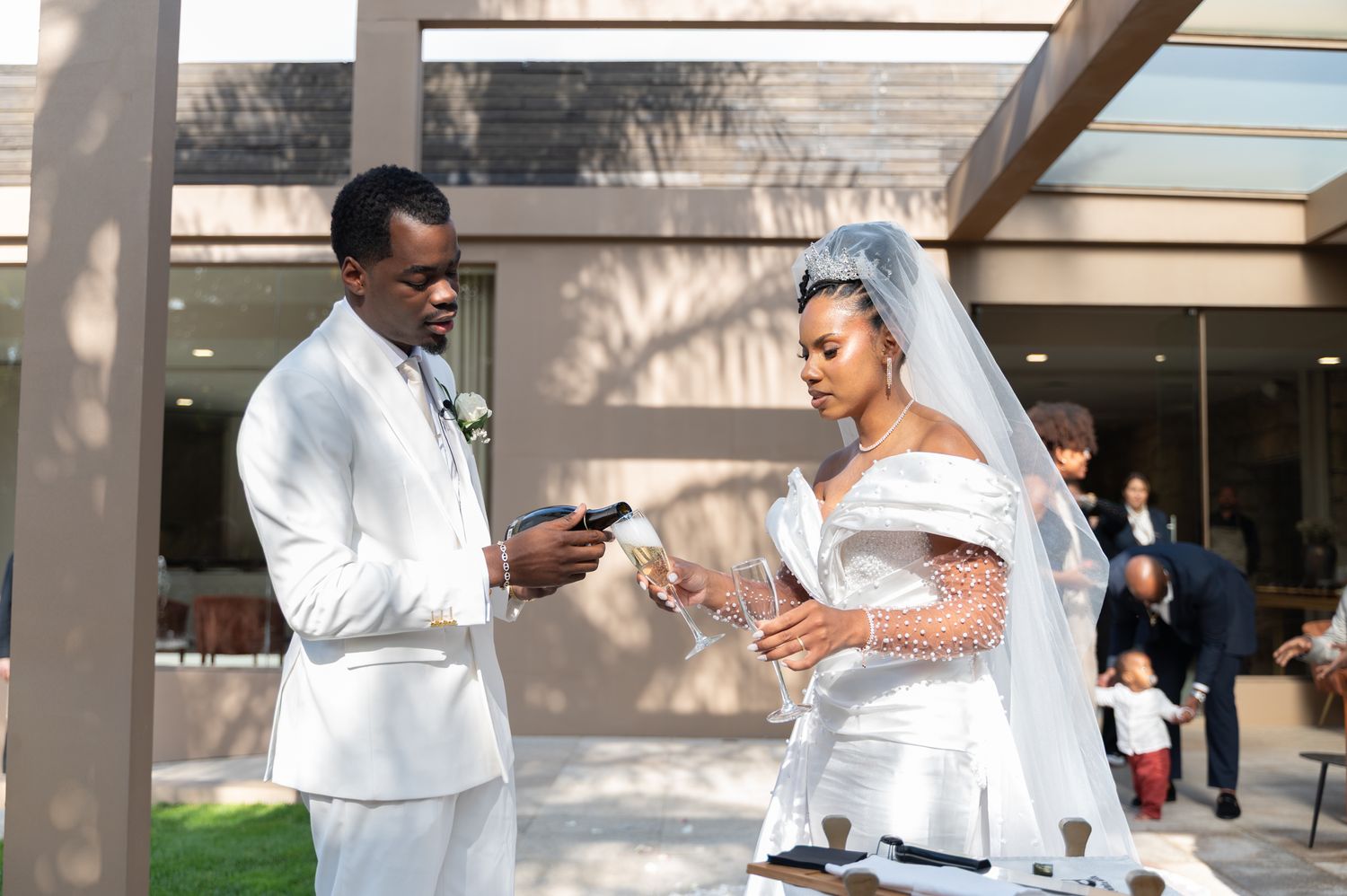 Bride and groom performing unity ceremony ritual outdoors in white wedding attire.