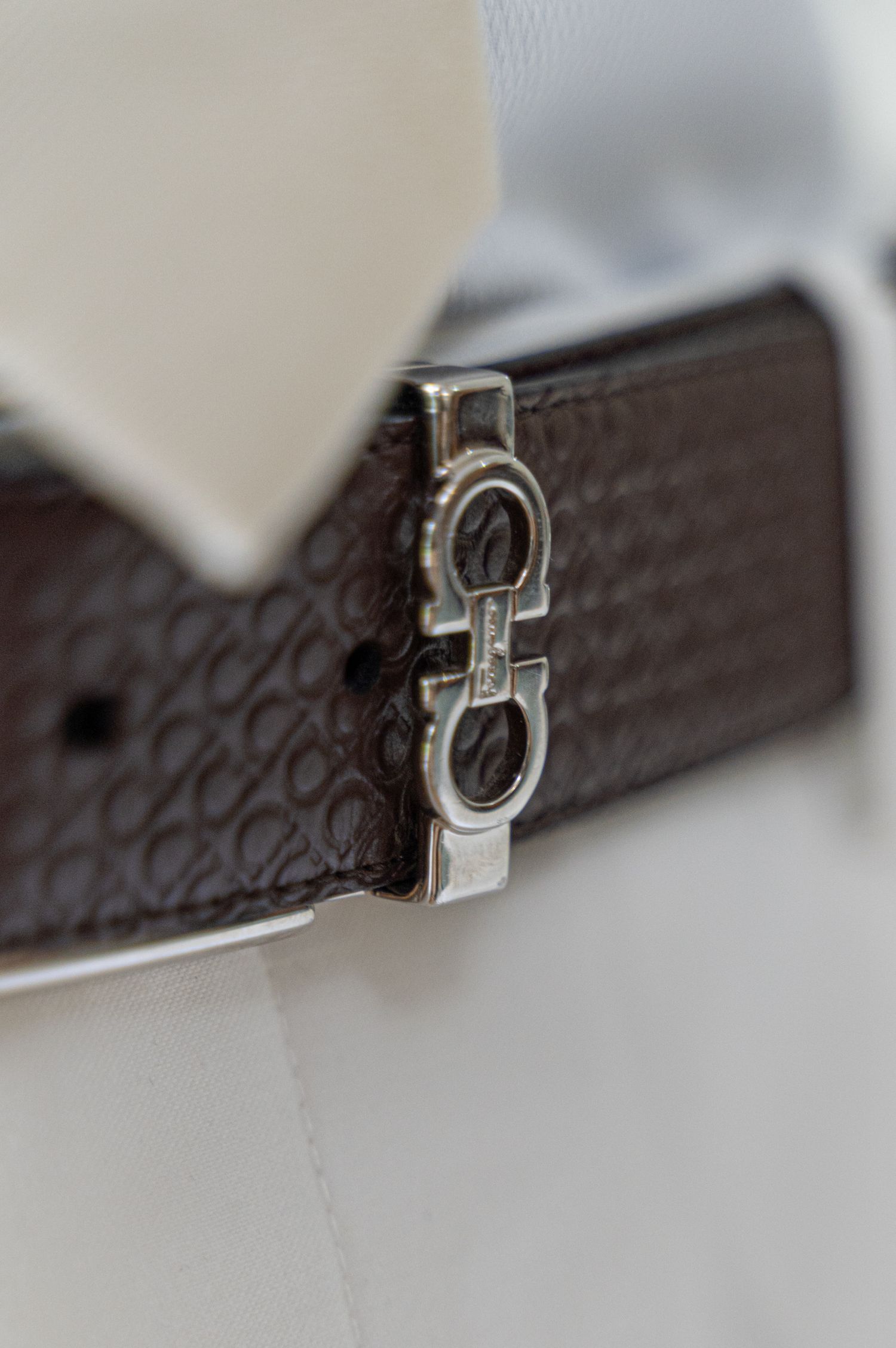 Close-up of a dark brown Salvatore Ferragamo belt buckle against white dress shirt and cream tie.