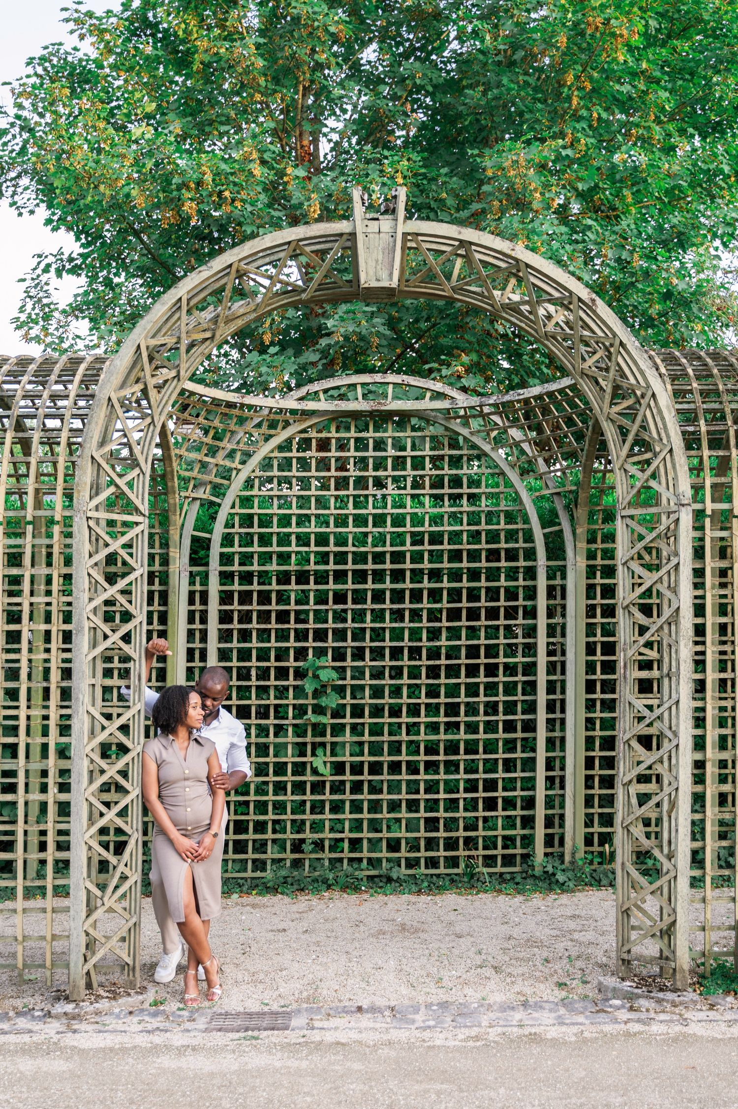 Couple embracing under ornate garden arch trellis covered in lush green foliage.