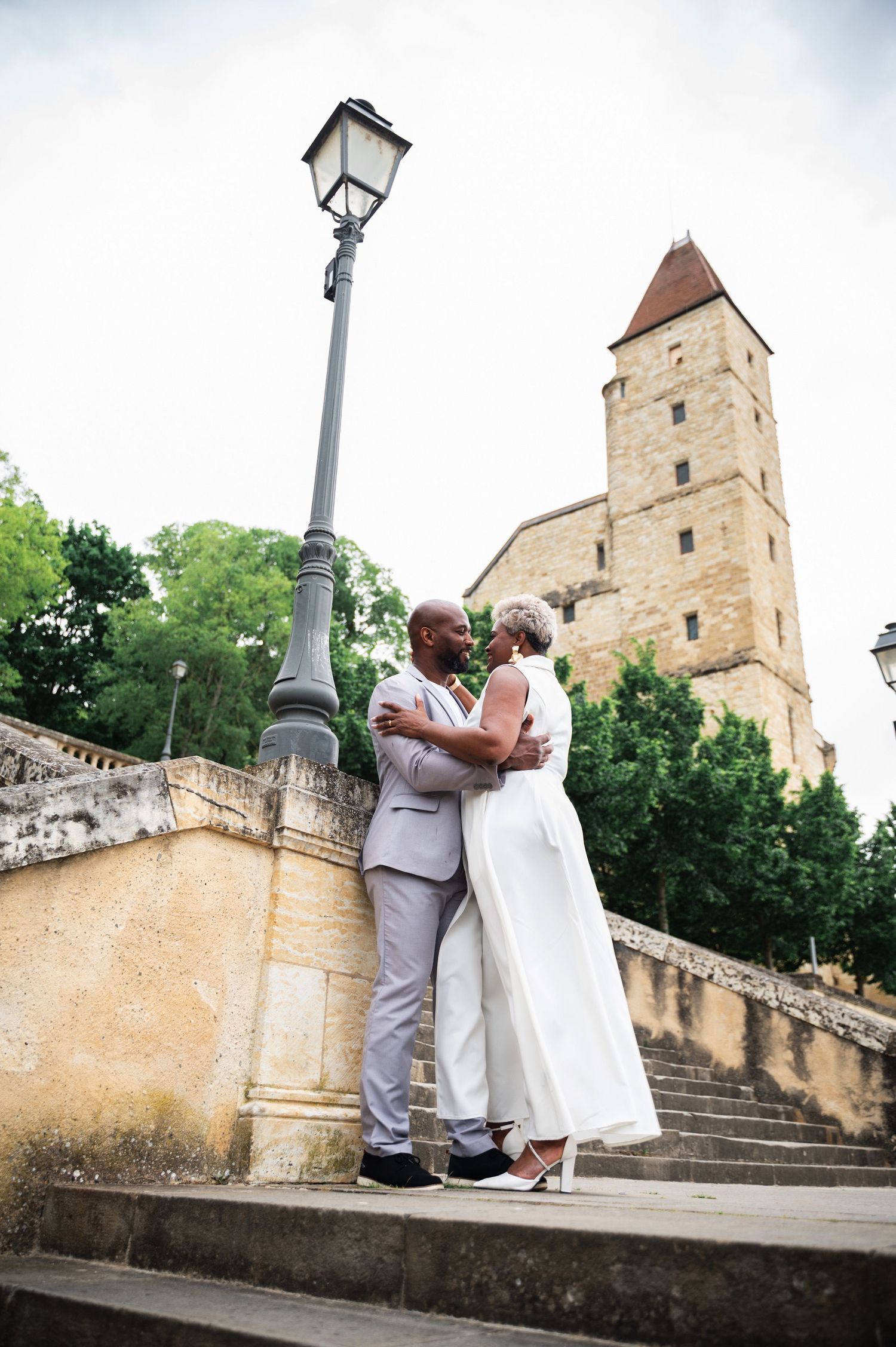Black couple sharing a romantic moment on stone steps near a lamppost with historic tower behind them.