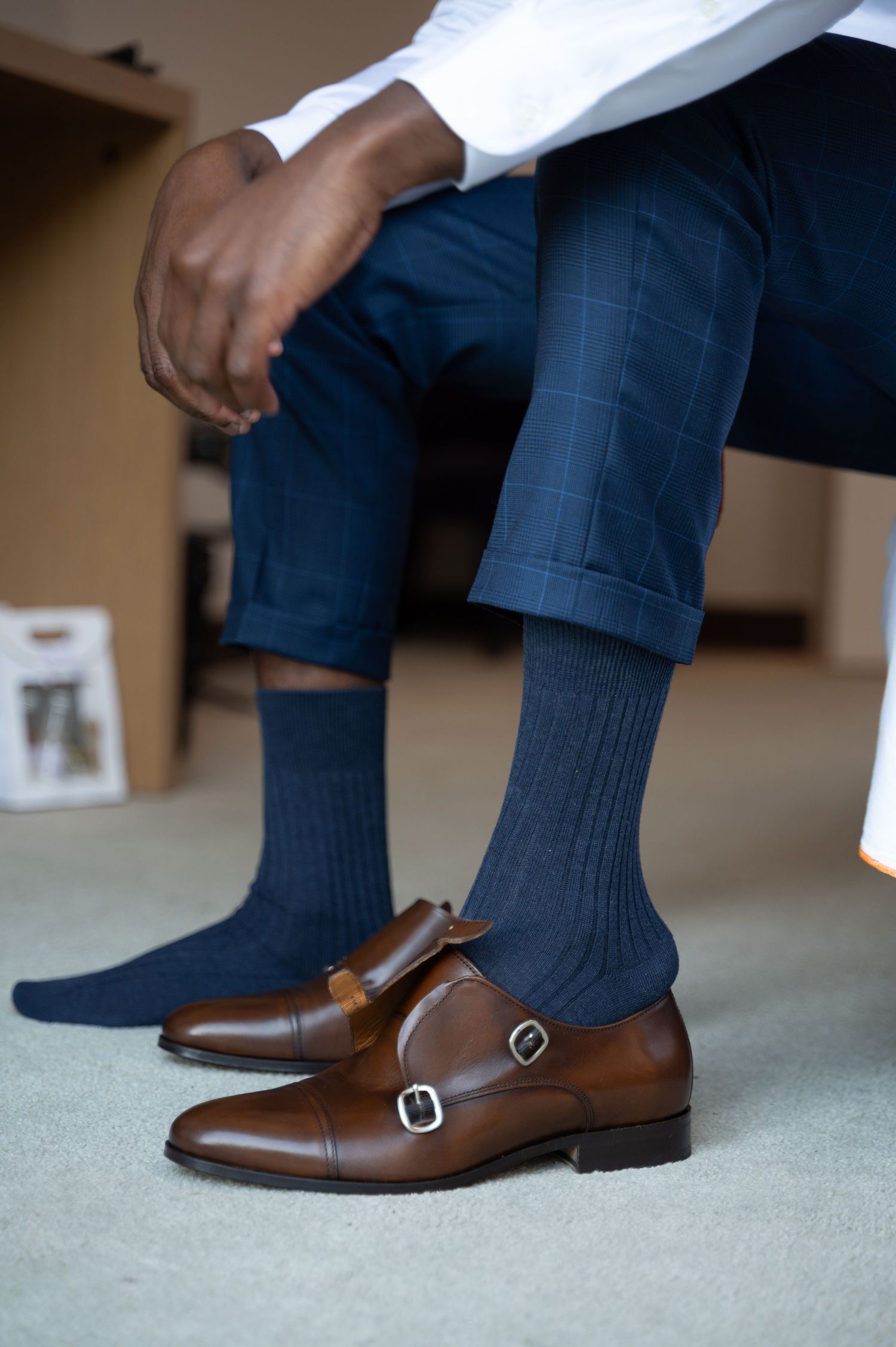 Close-up of brown leather double monk strap shoes with navy blue dress socks and checkered trousers.