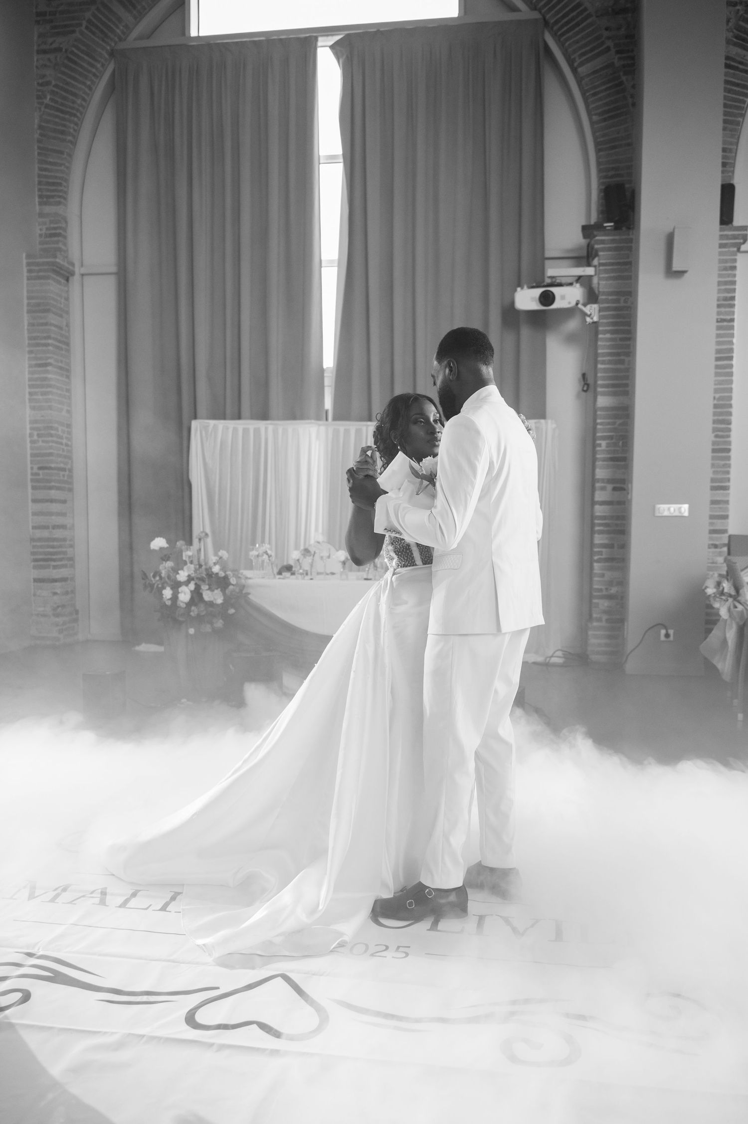 Black and white photo of bride and groom sharing first dance surrounded by fog at wedding reception.
