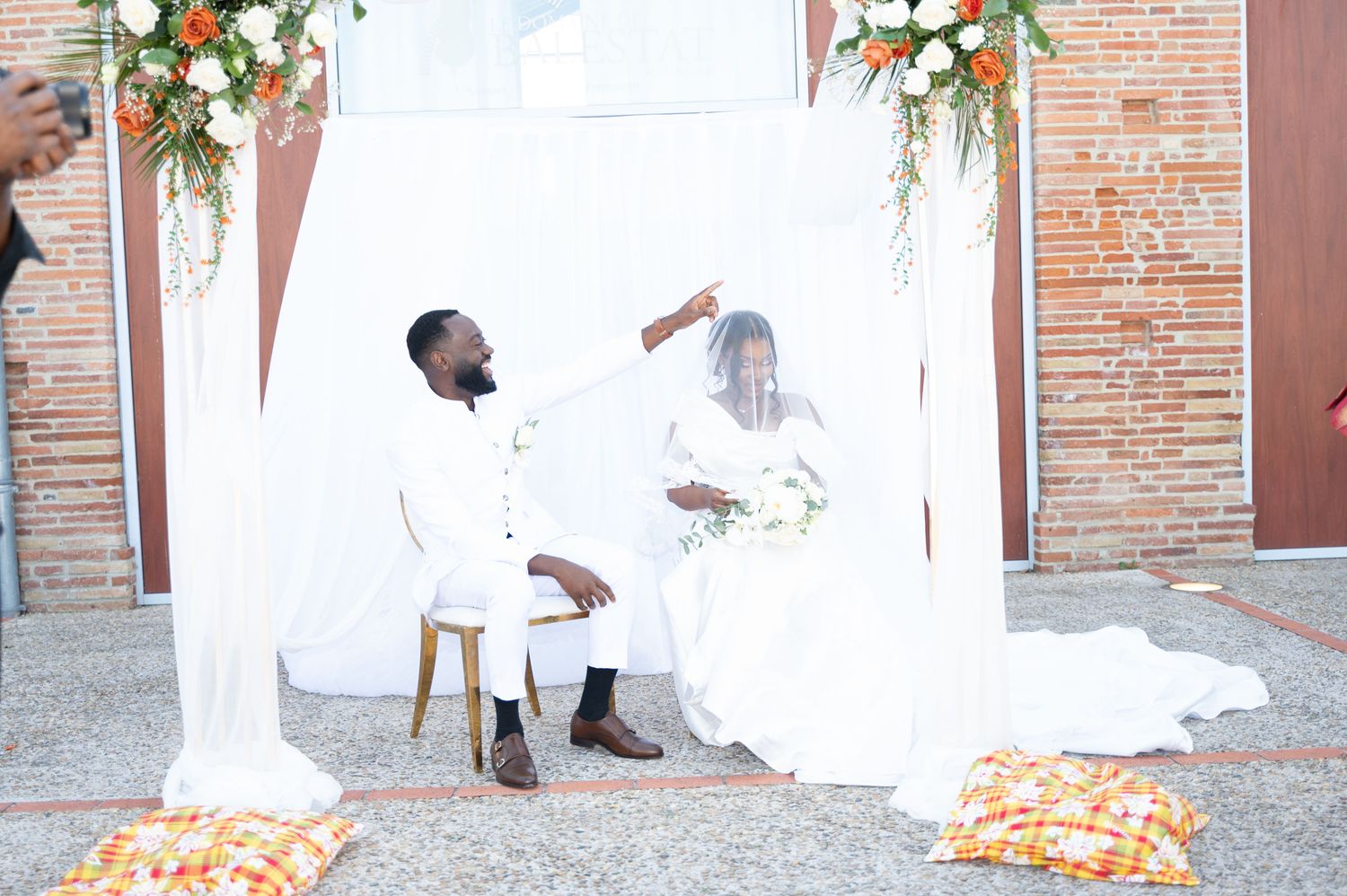 Bride and groom share joyful moment under white canopy with orange floral decorations.