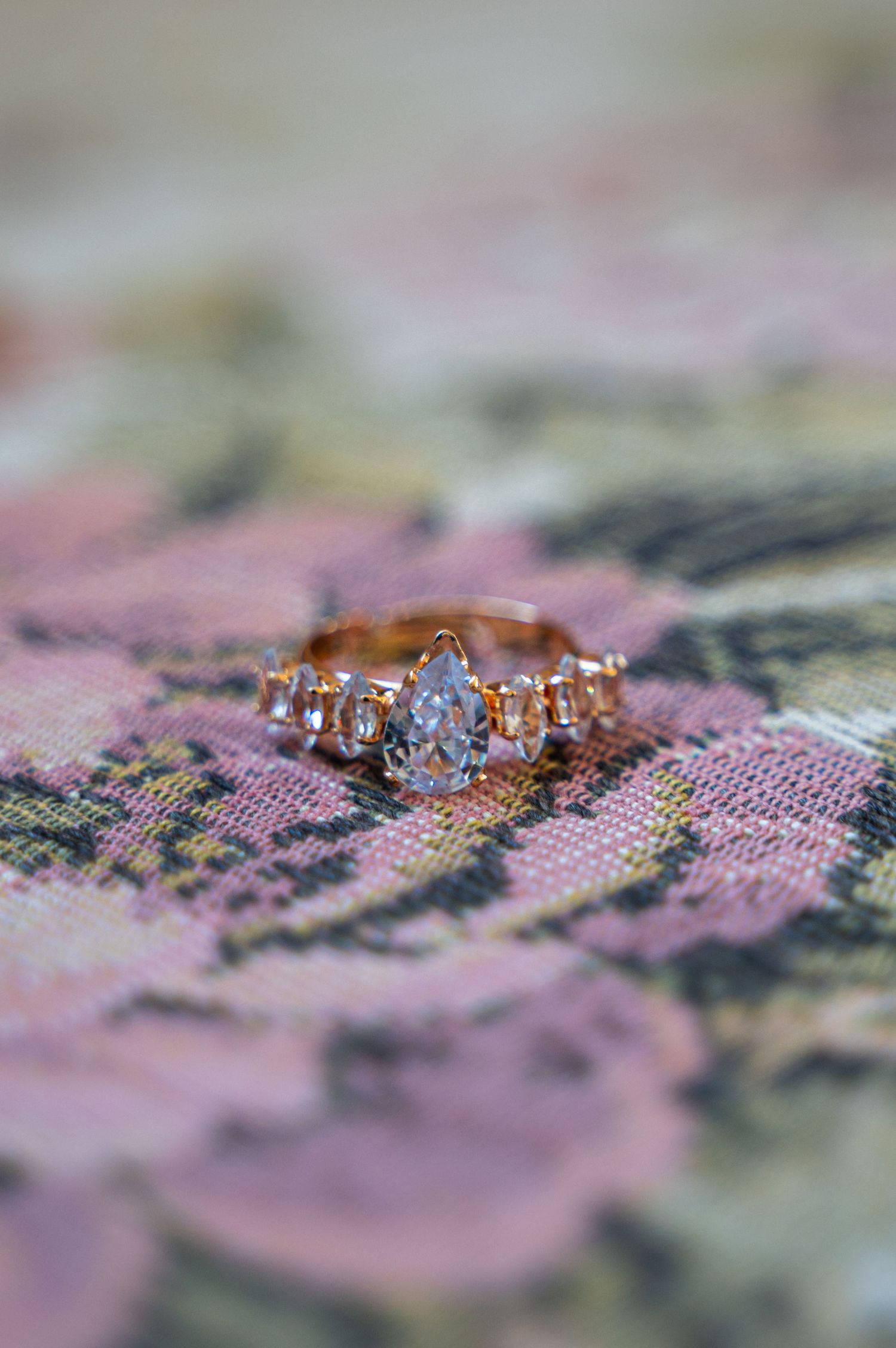Rose gold pear-shaped diamond engagement ring with side stones on floral fabric background.
