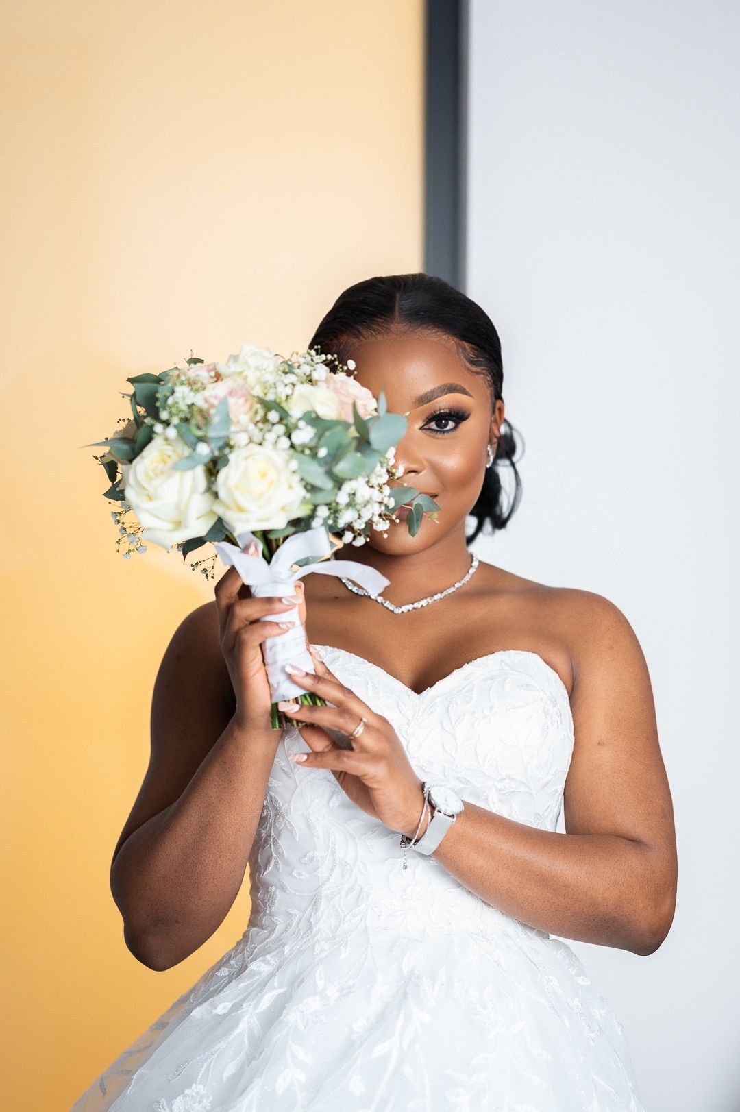Elegant Black bride in strapless lace gown holding white and pink rose bouquet near her face.