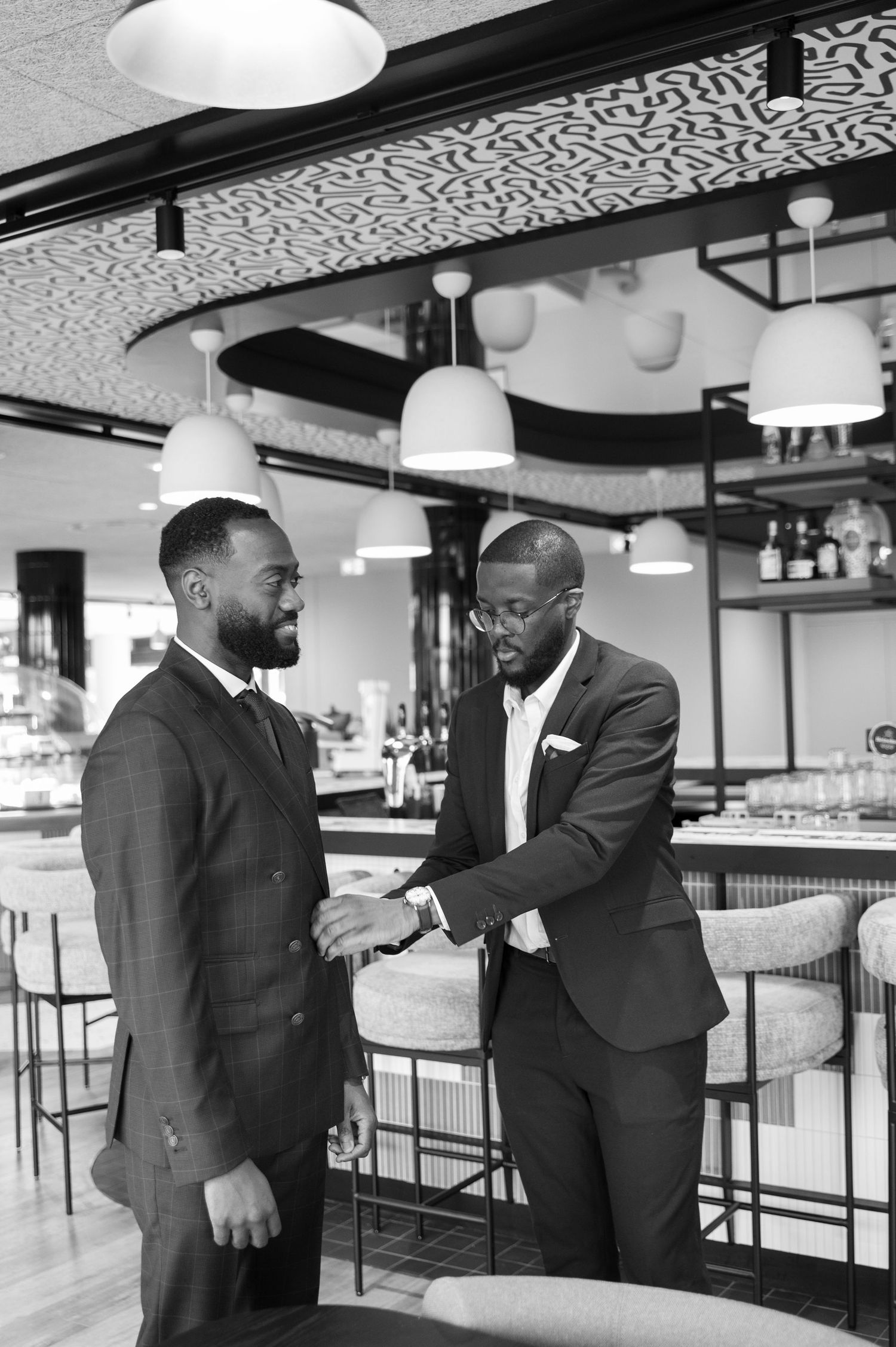 Black and white photo of two Black men in suits sharing a handshake in an elegant bar setting.