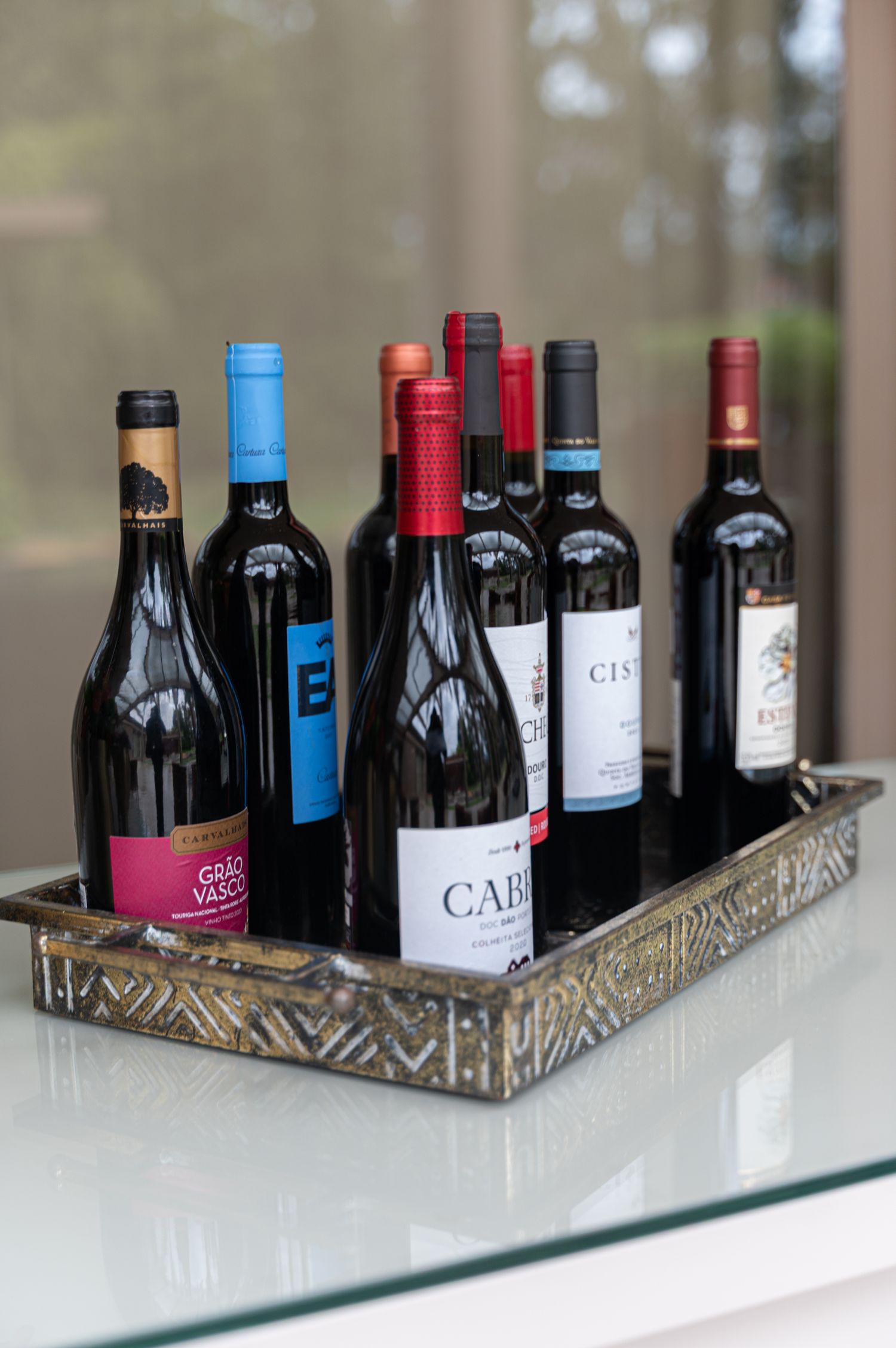 Collection of red wine bottles displayed on decorative tray on glass surface.