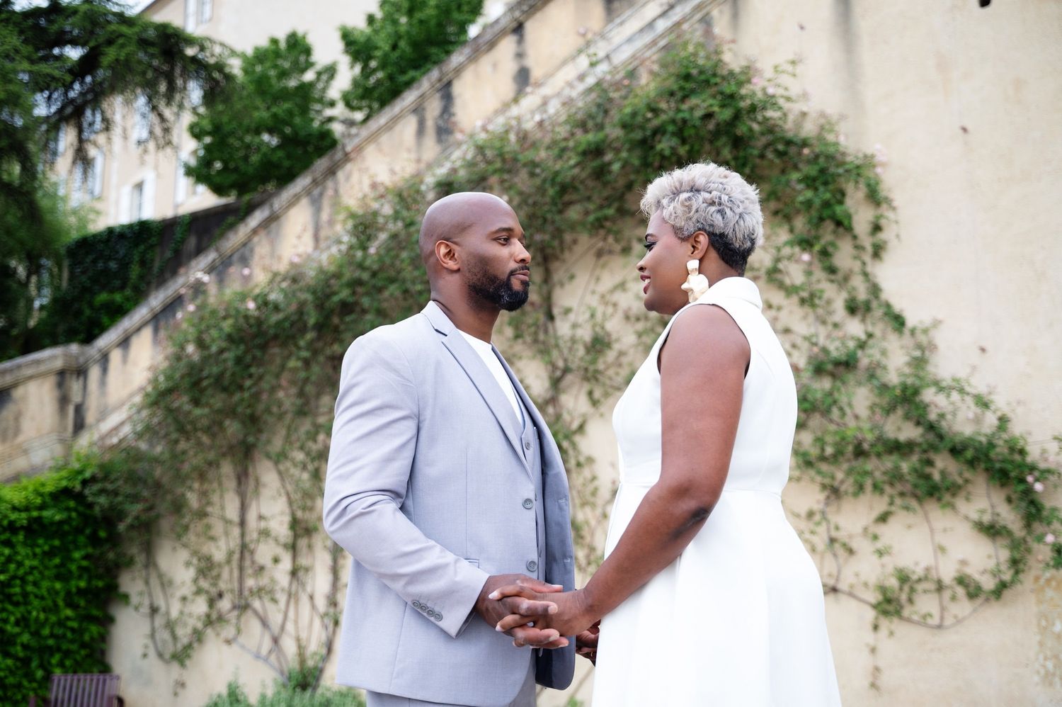 Black couple holding hands and gazing at each other in front of an ivy-covered stone wall.