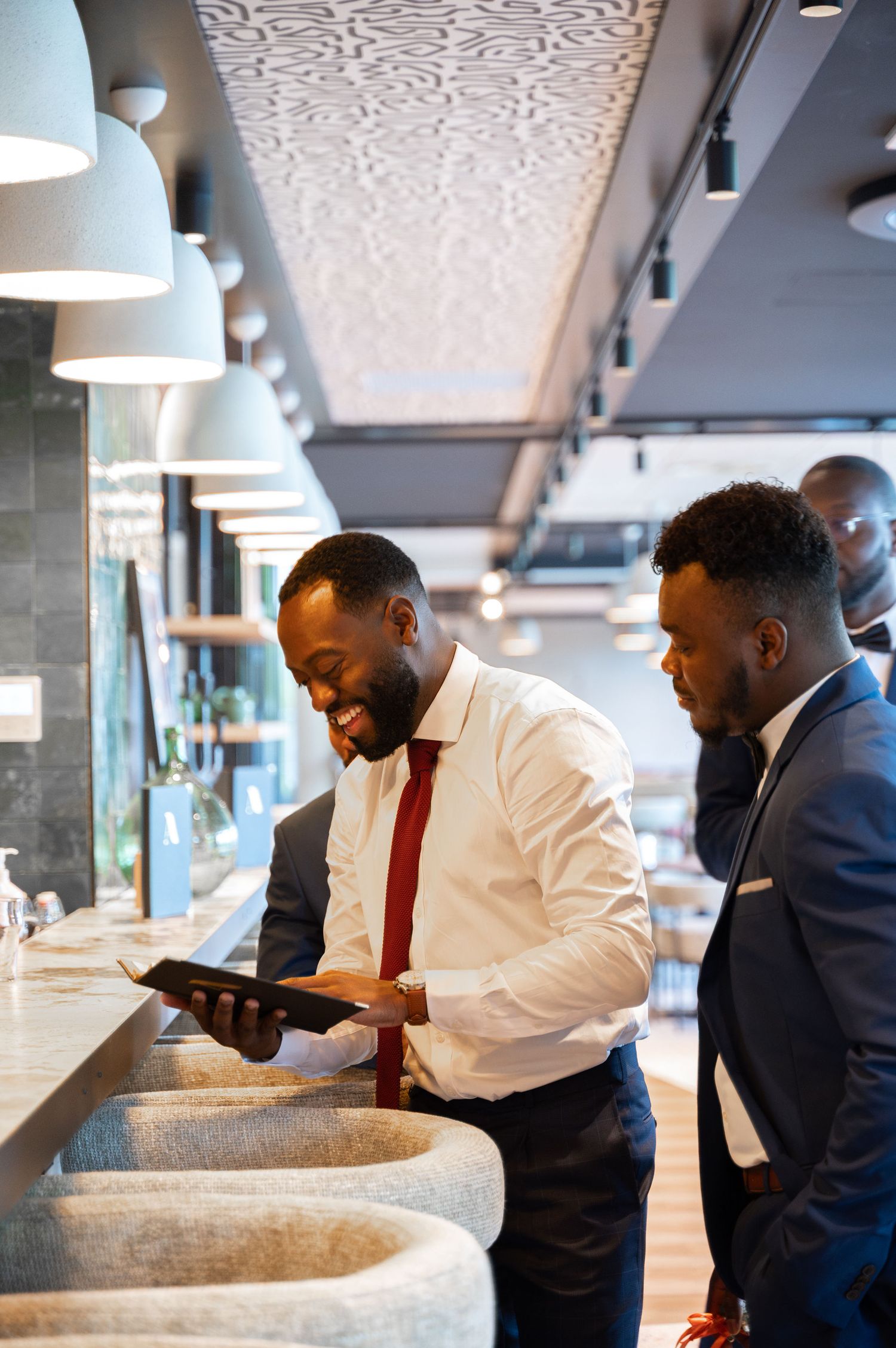 Two Black men in suits review a tablet together at a contemporary restaurant bar counter.