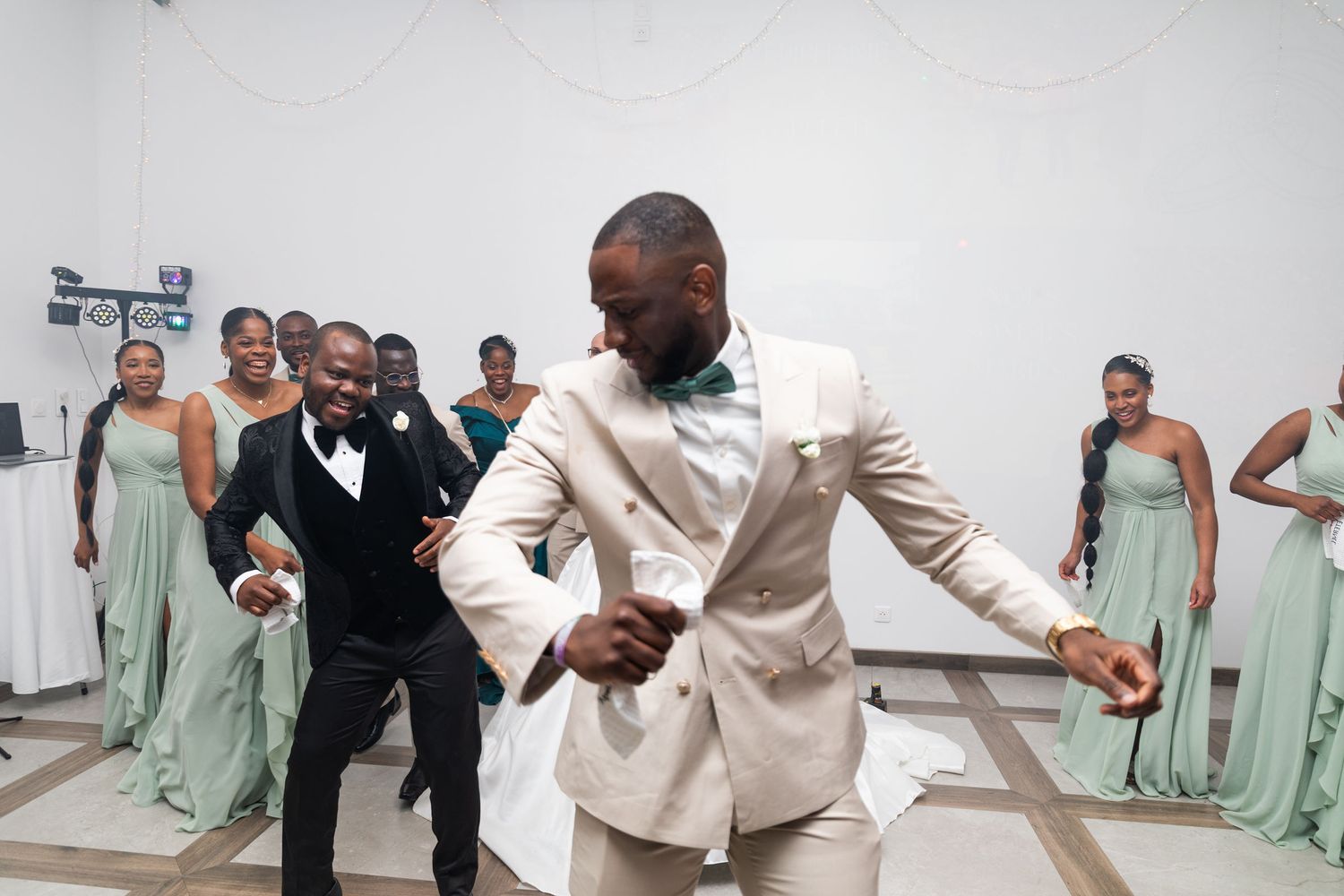 Groomsmen dancing energetically at wedding reception with bridesmaids in sage green gowns.