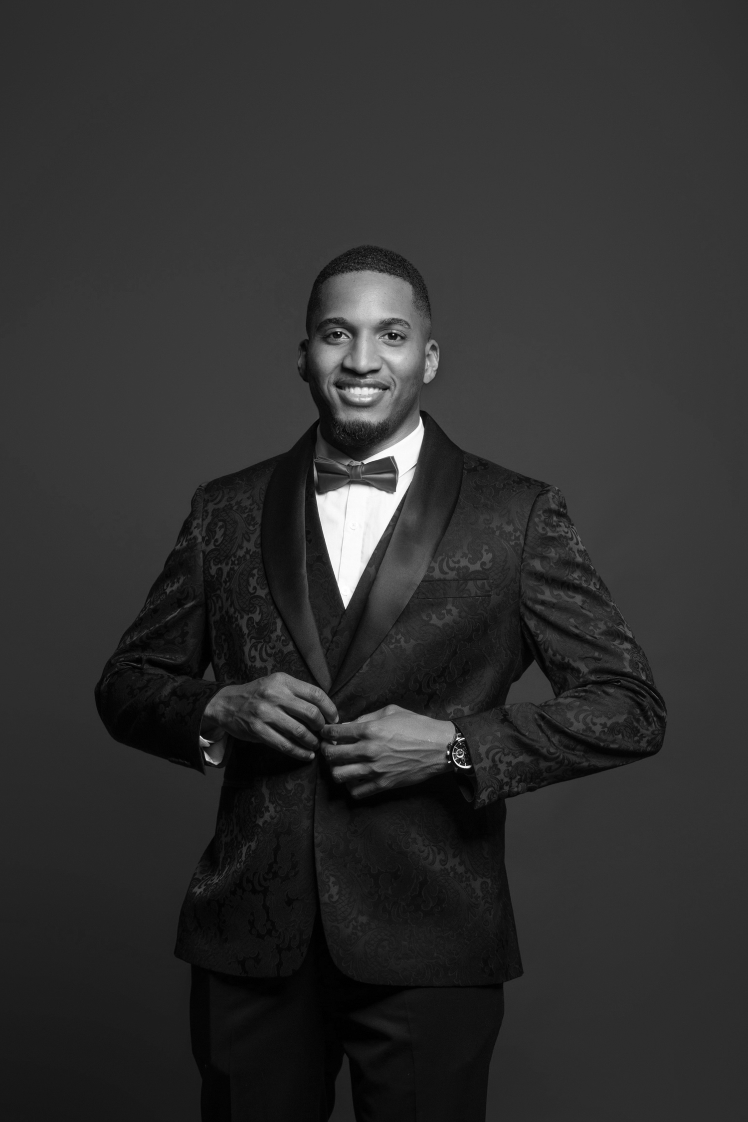Black and white portrait of a smiling groom in a patterned tuxedo adjusting his jacket.