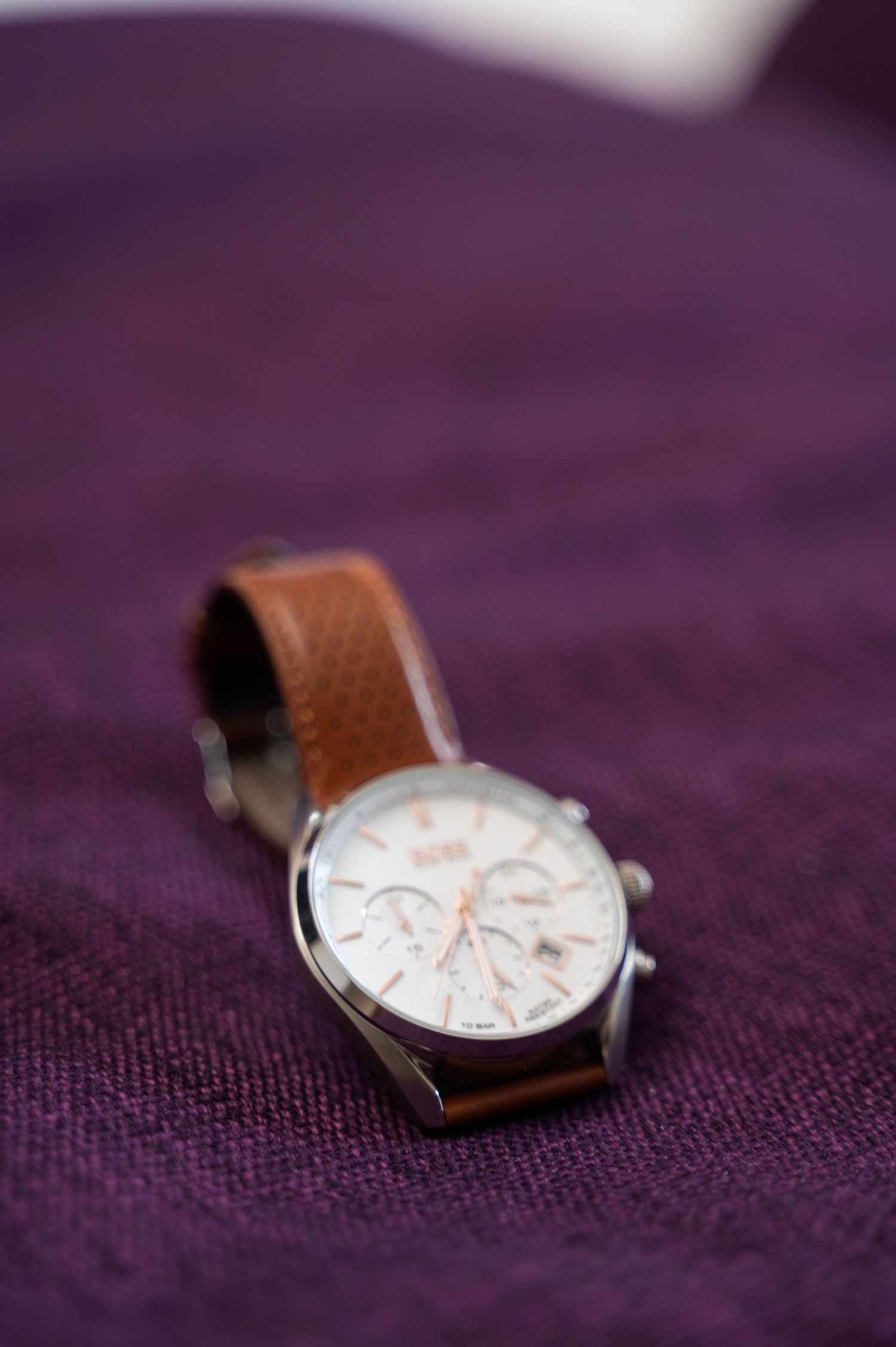Elegant mens brown leather strap chronograph watch resting on purple fabric for groom wedding day details.