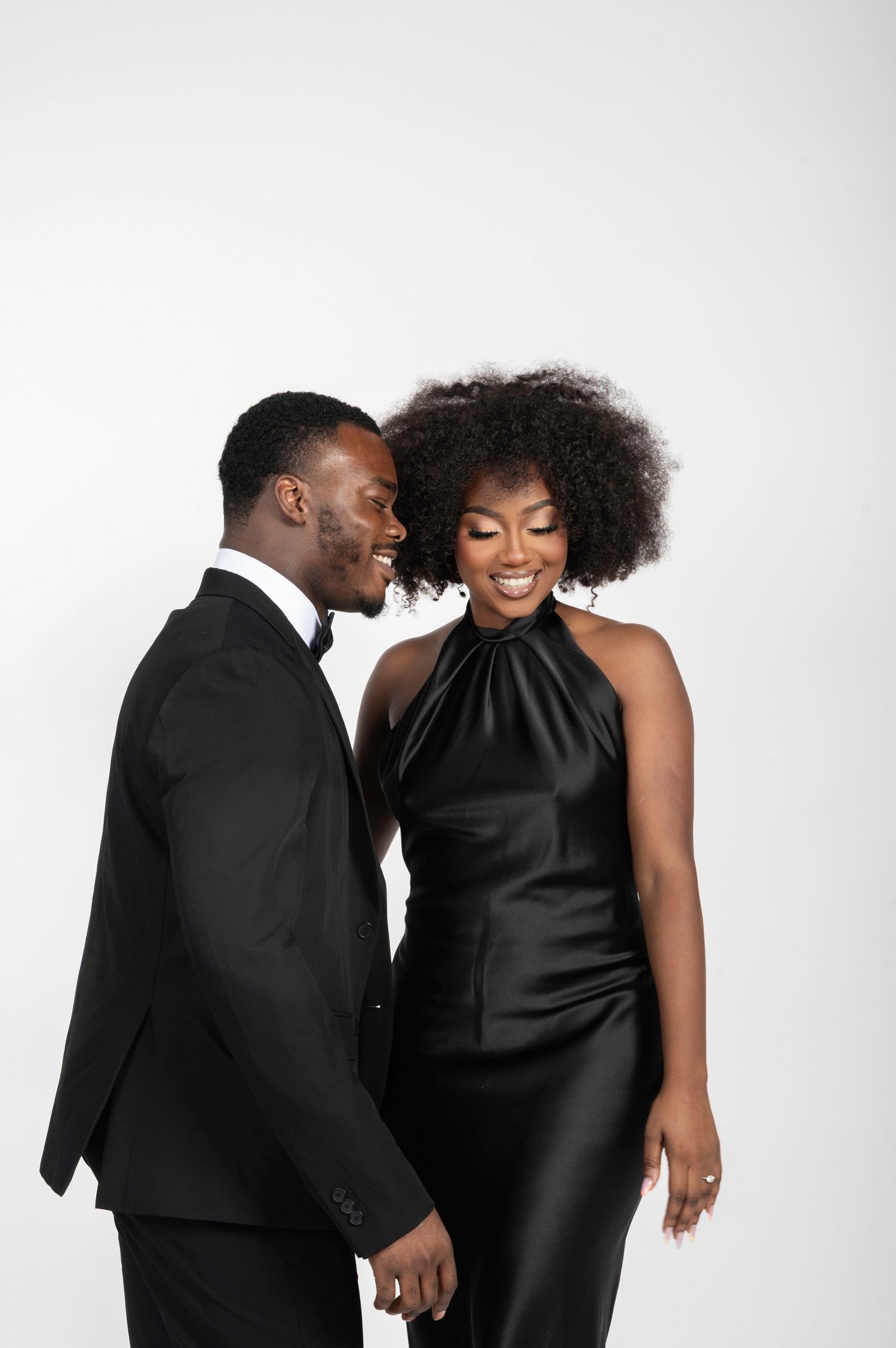 Stylish Black couple in matching black formal wear, man in suit and woman in satin halter dress, smiling together.