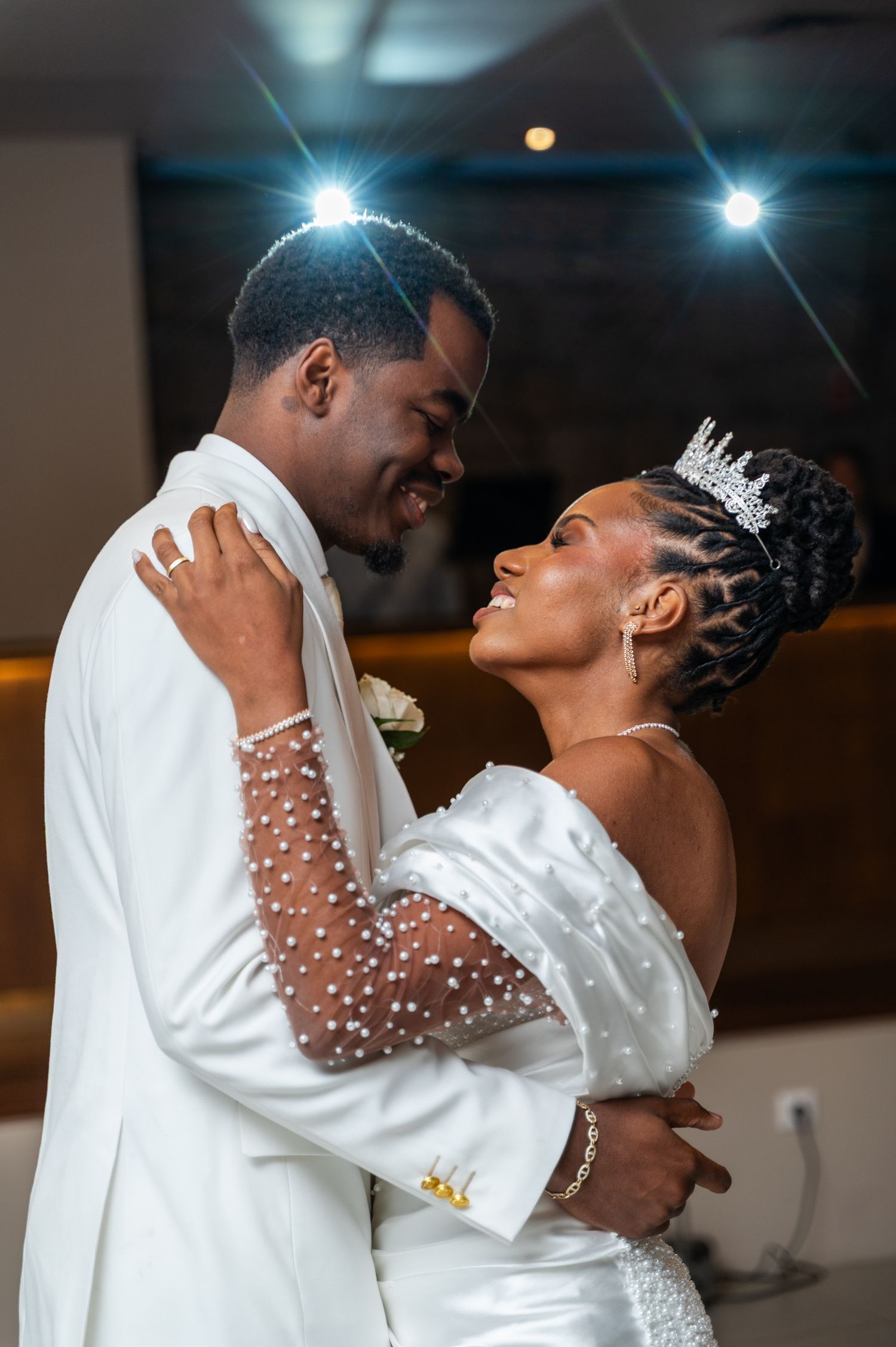 Newlyweds share a joyful first dance embrace, bride wearing a sparkling crown and pearl-sleeve wedding gown.