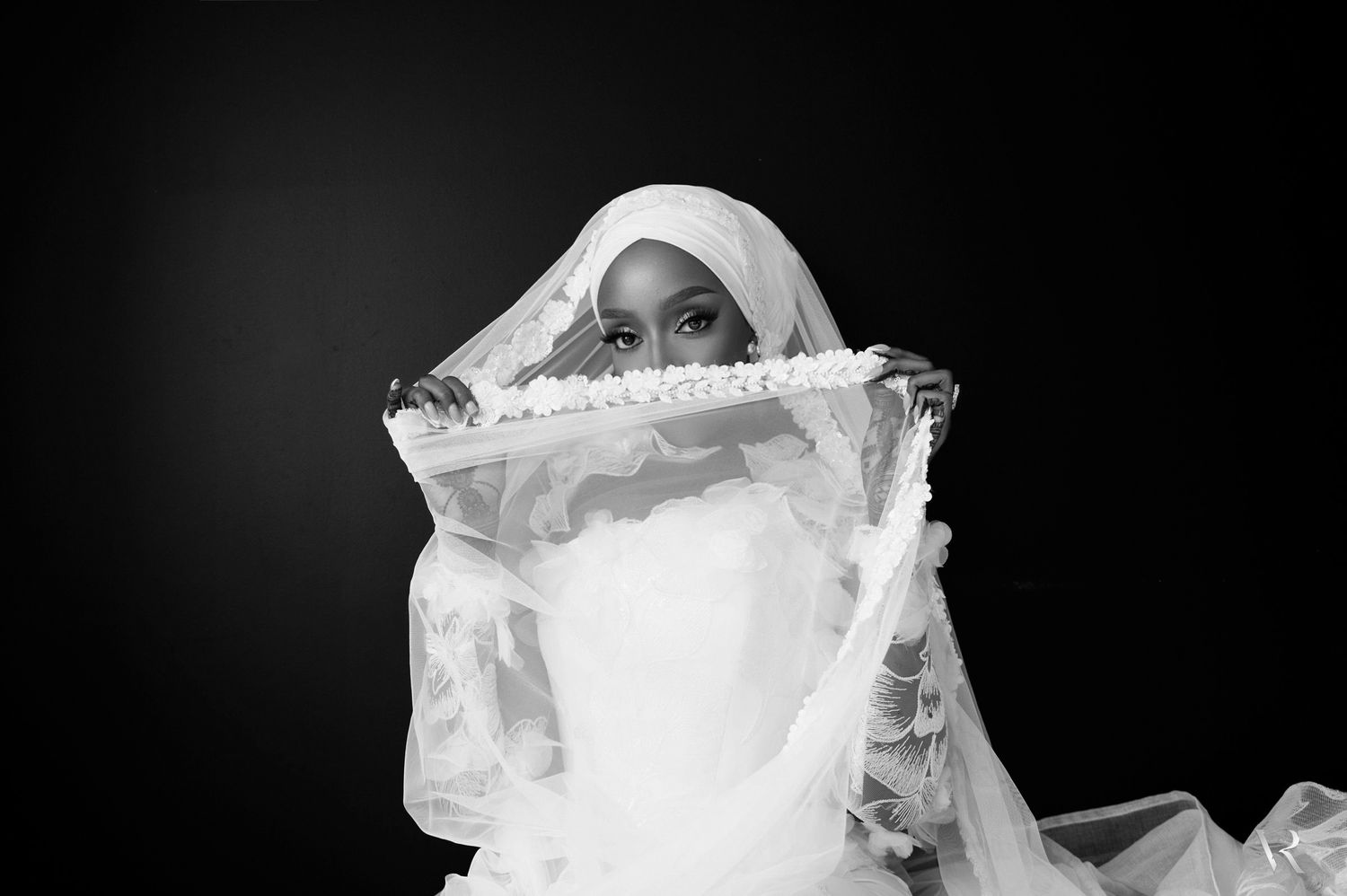 Black and white portrait of a woman in a white bridal veil holding a decorative fan near her face.