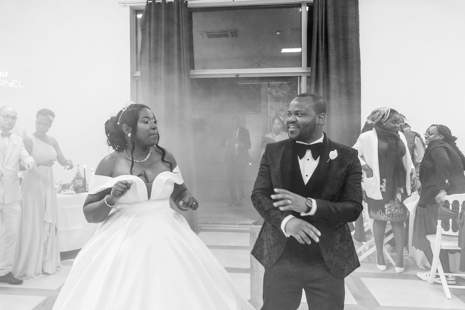 Bride in ball gown and groom in tuxedo make grand entrance at wedding reception in black and white.