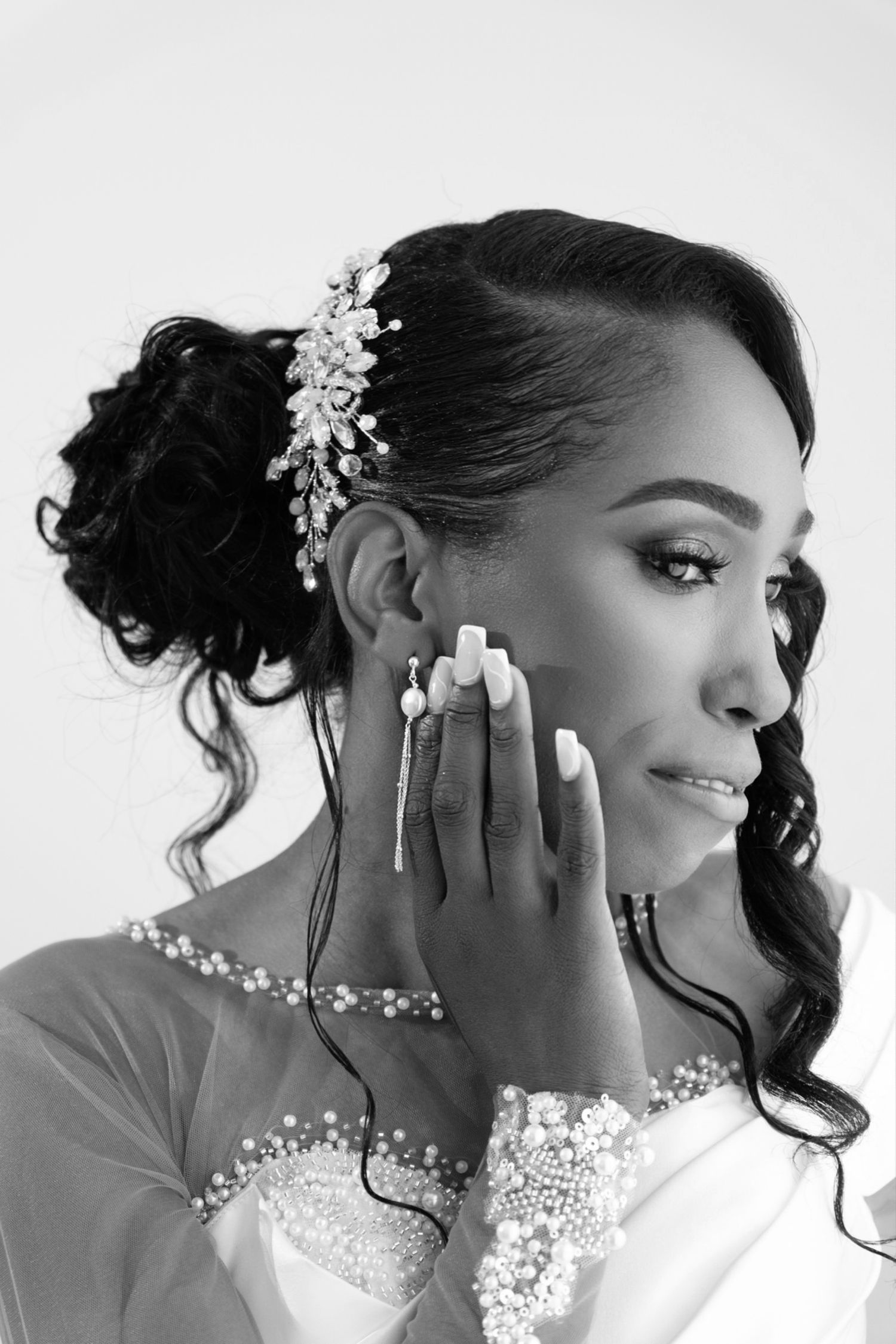Black and white portrait of a bride with pearl hair accessory and intricate lace sleeve details.