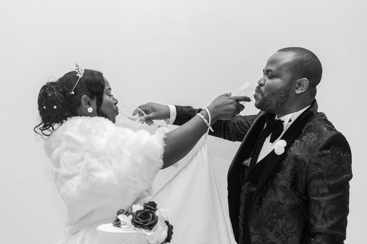 Black and white photo of bride playfully feeding wedding cake to groom at reception celebration.