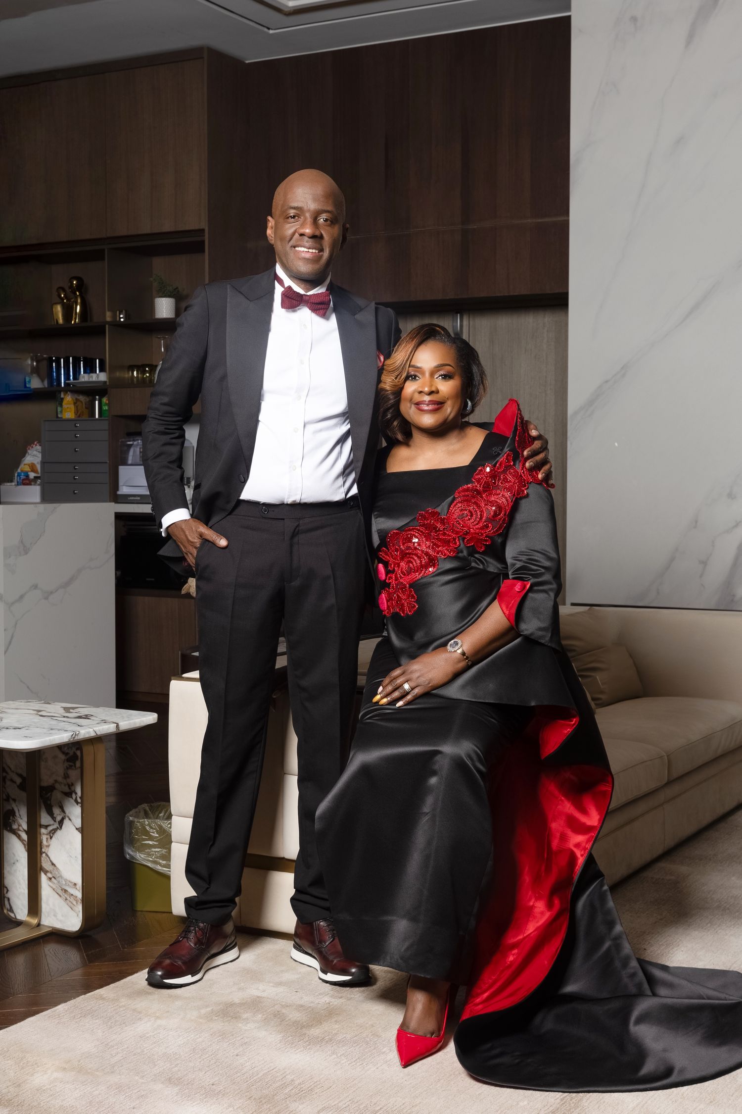 Elegant Black couple poses in luxurious interior, man in tuxedo, woman in black and red gown.
