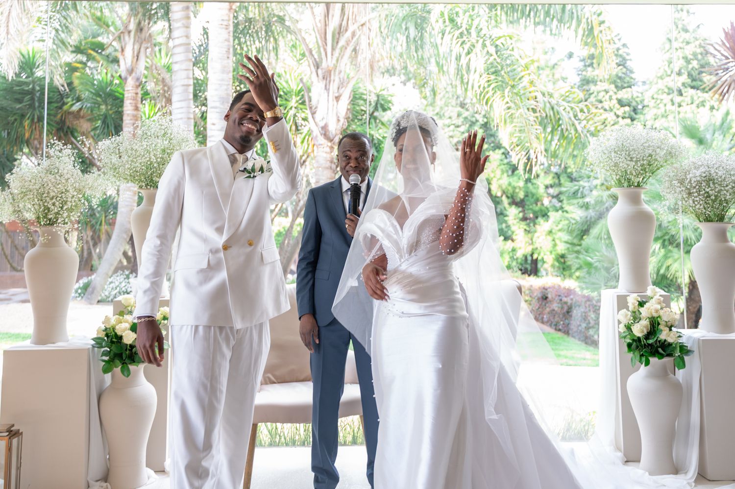 Joyful newlyweds celebrate with raised hands at altar flanked by white floral arrangements.
