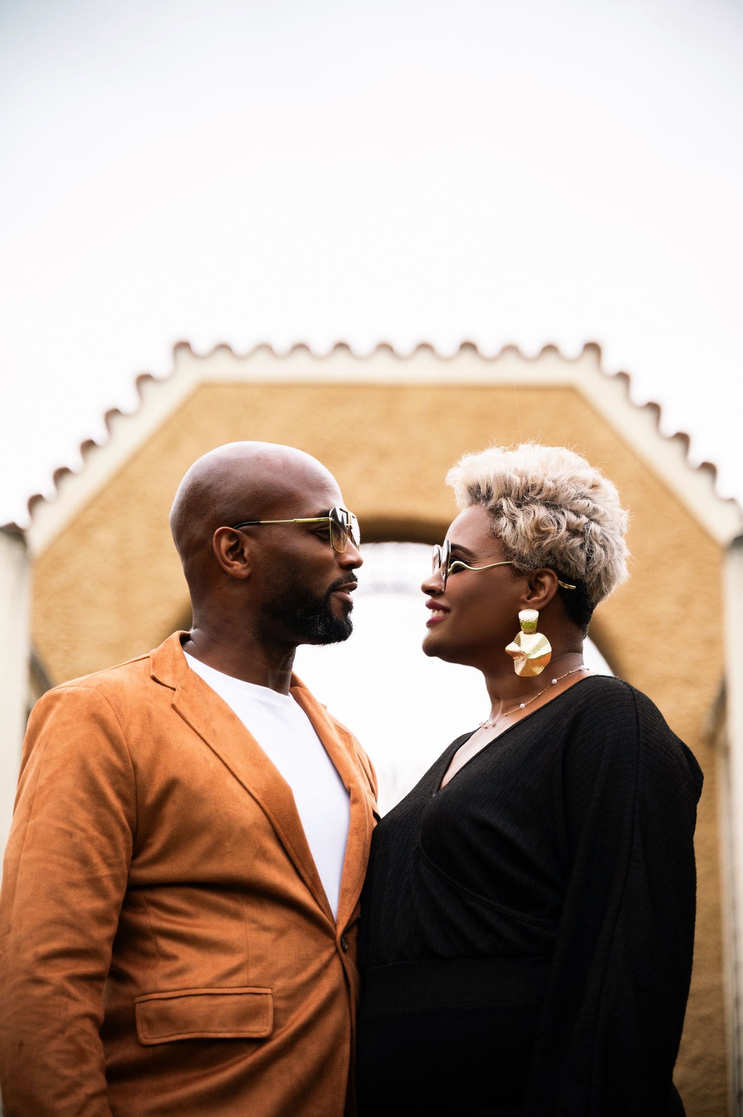 Stylish couple in sunglasses facing each other outdoors with a building behind them.