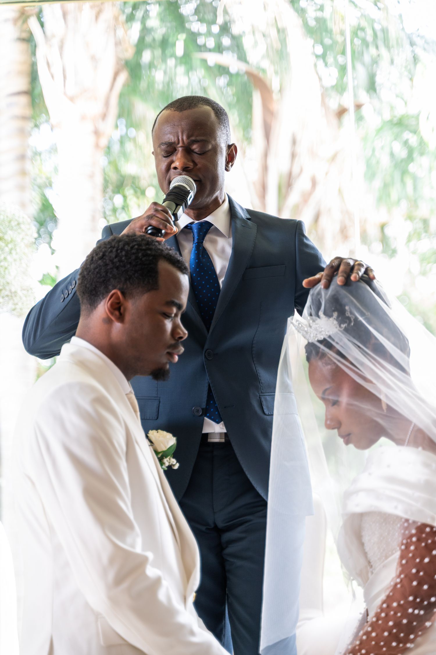 Officiant prays over bowing groom and bride during solemn wedding blessing ceremony.