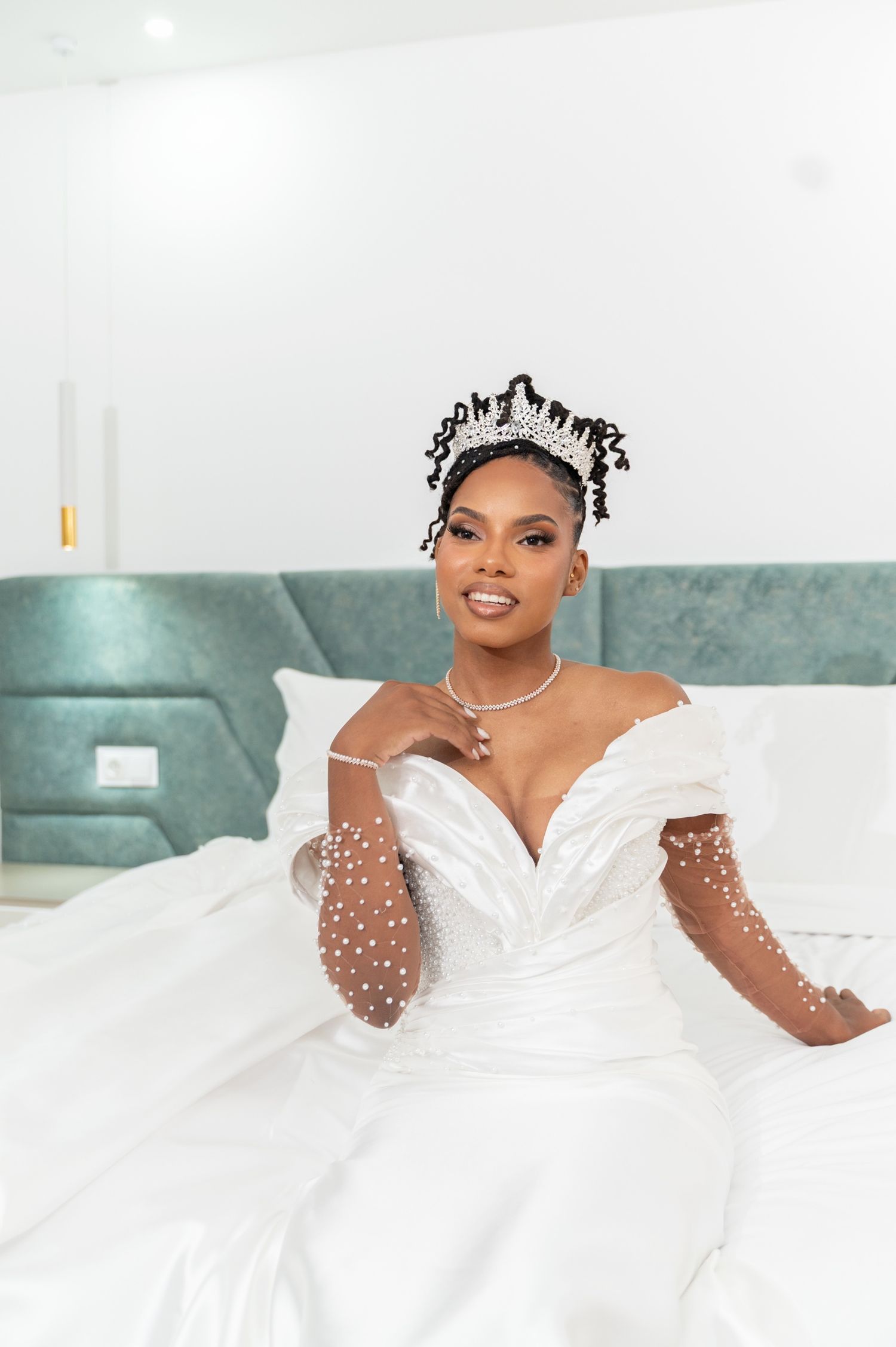 Radiant Black bride smiling in off-shoulder pearl wedding dress and sparkling tiara.
