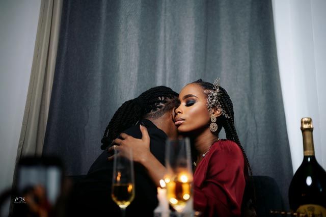 Couple sharing a romantic kiss at candlelit dinner table with champagne glasses and bottle in elegant setting.