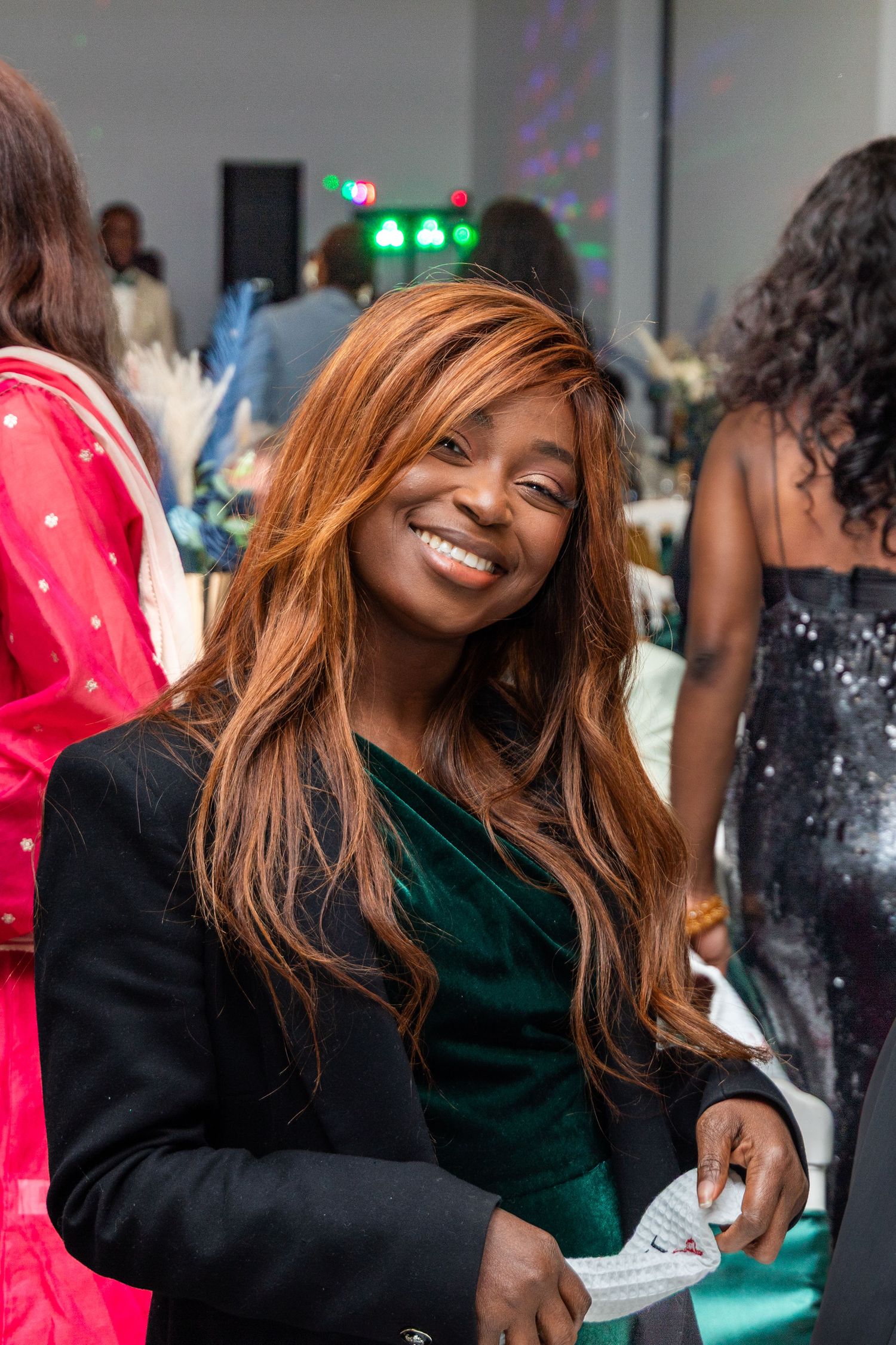 Woman with long auburn hair smiles warmly in green velvet dress at a festive wedding reception.