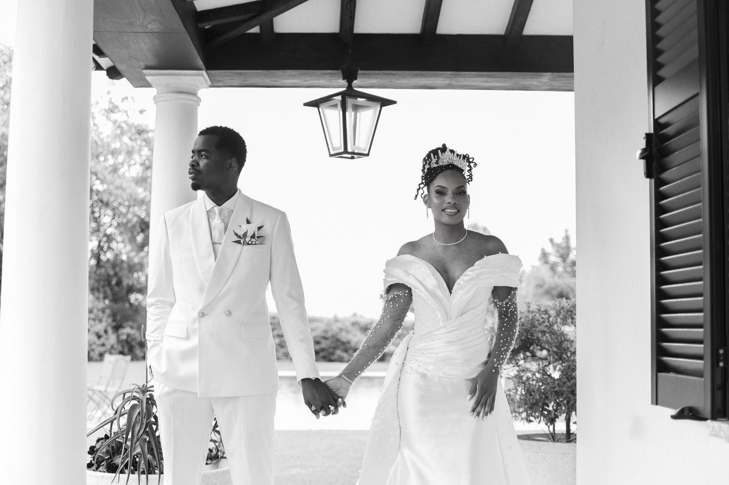 Black and white photo of a bride and groom holding hands under a columned portico on their wedding day.