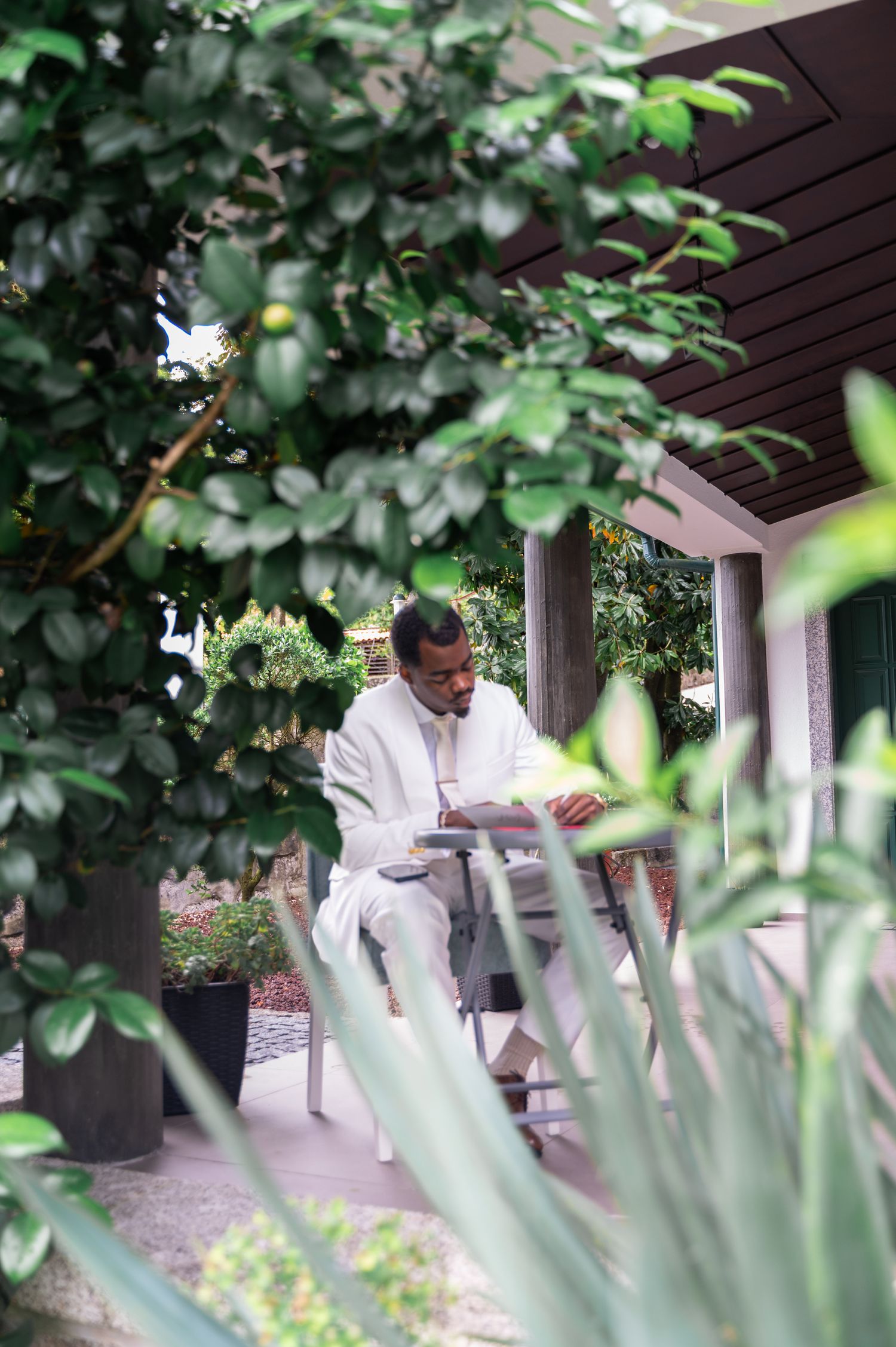 Groom in white suit reading vows while seated outdoors surrounded by lush green foliage.