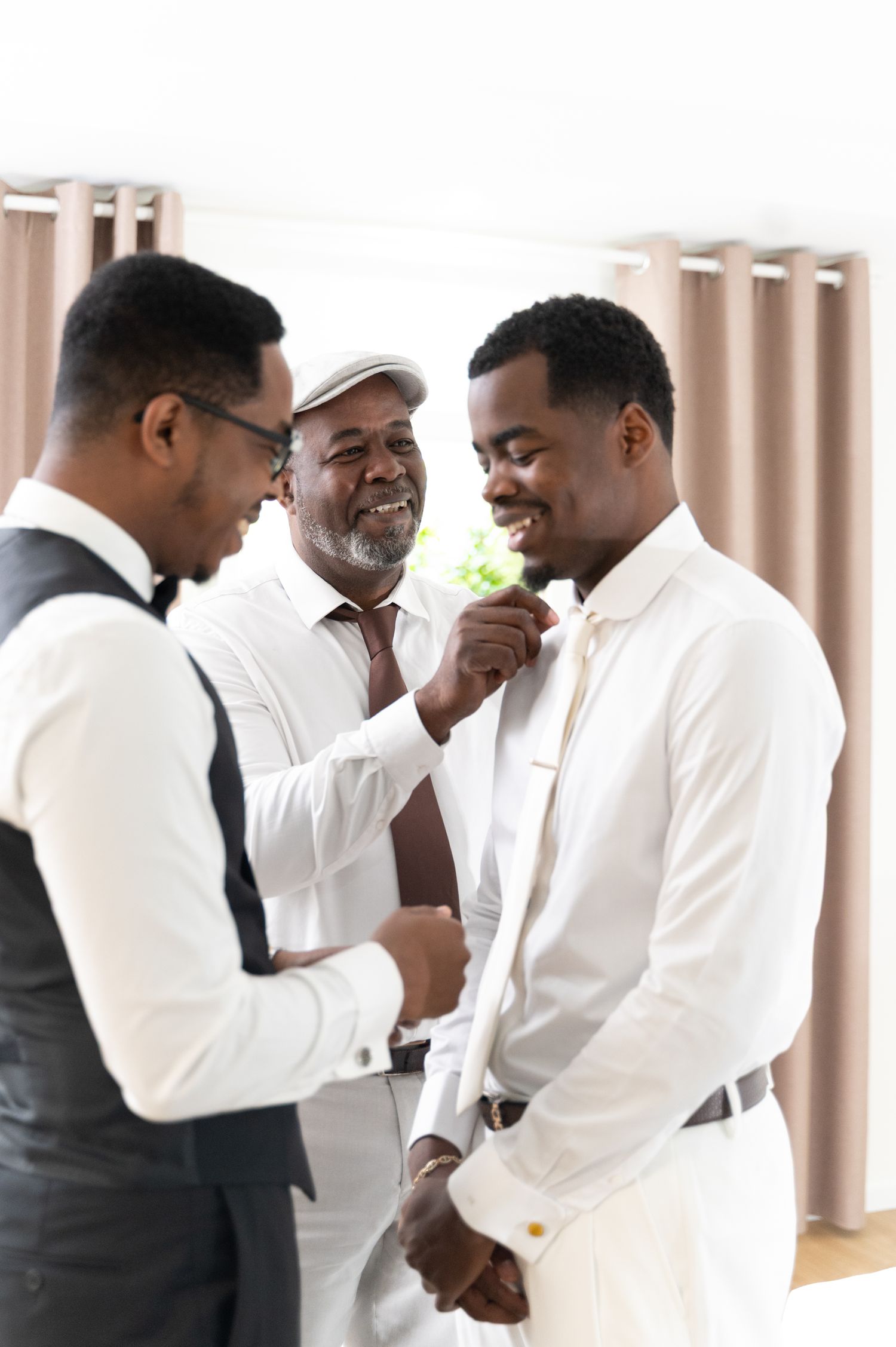 Three men in white suits helping groom with boutonniere during wedding preparations.