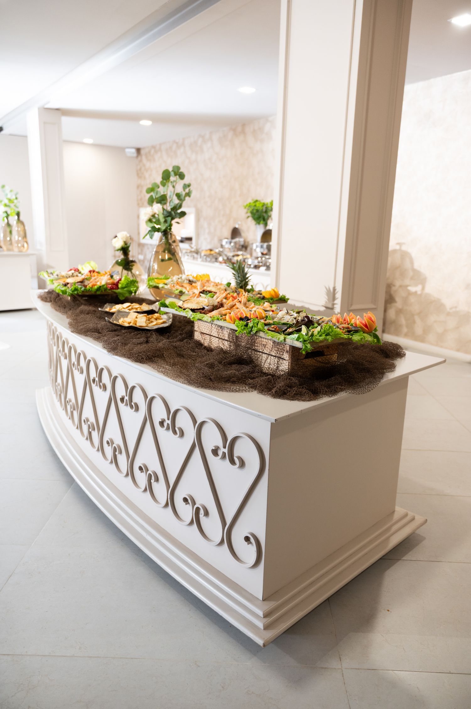 Ornate white buffet table with decorative scrollwork featuring an elegant spread of food at a formal event.