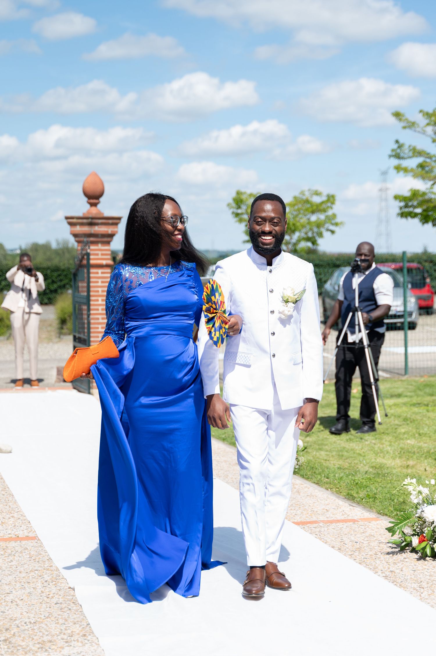 Couple walks down wedding aisle, woman in royal blue gown and man in white suit with bouquet.