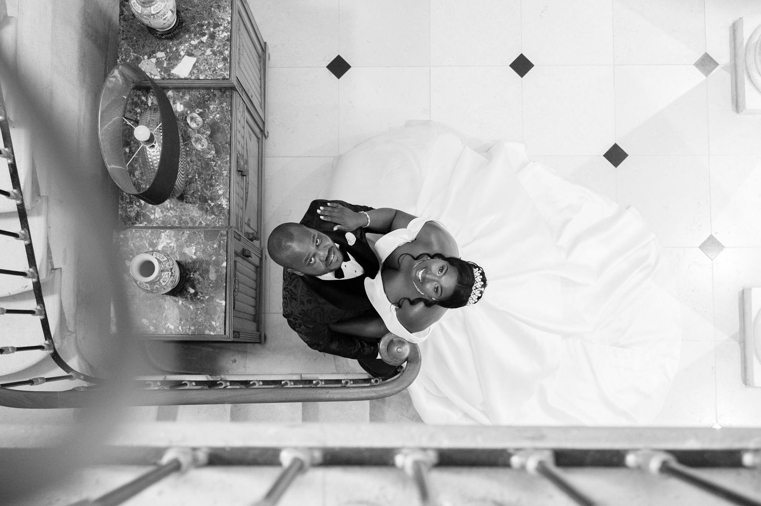 Black and white overhead photo of two men sitting together on a bed next to a vintage dresser.