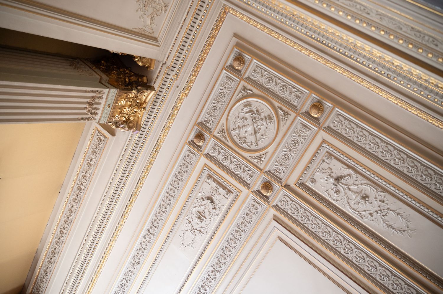 Ornate white and gold ceiling moldings with intricate classical architectural details in an elegant room.