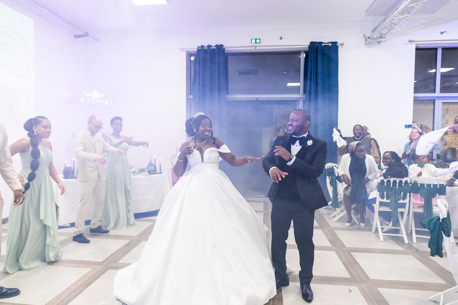 Bride and groom share first dance surrounded by guests and sage green bridesmaids.