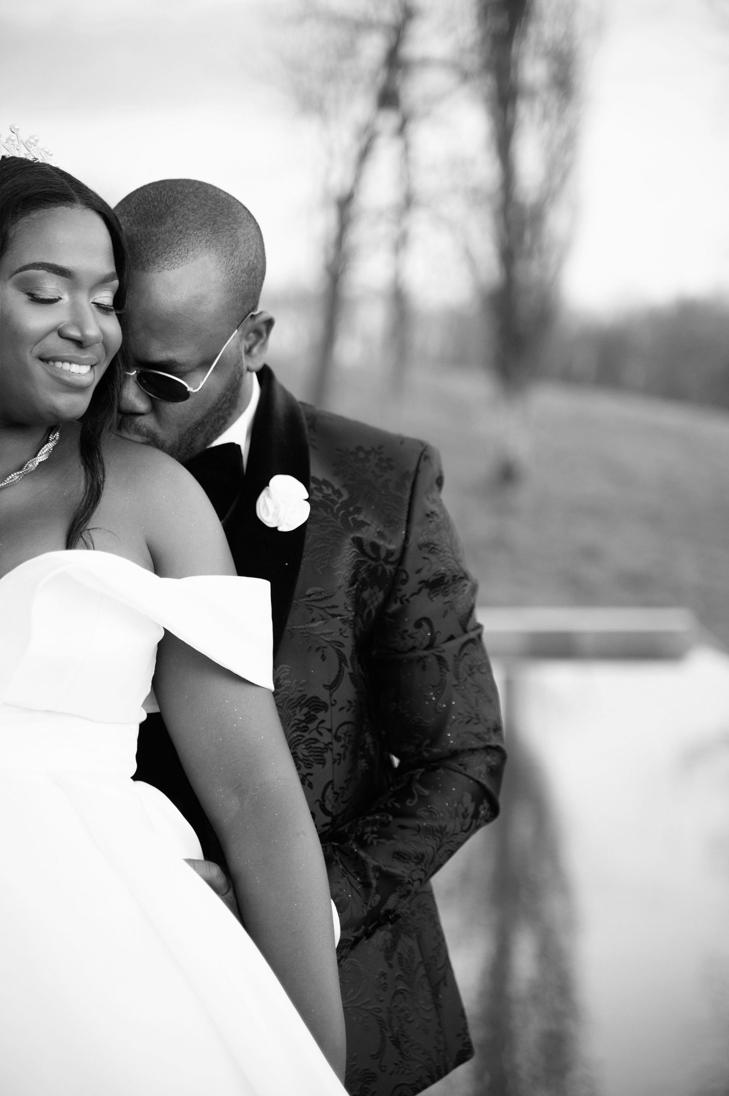Romantic black and white photo of groom in patterned suit nuzzling smiling bride in strapless gown.
