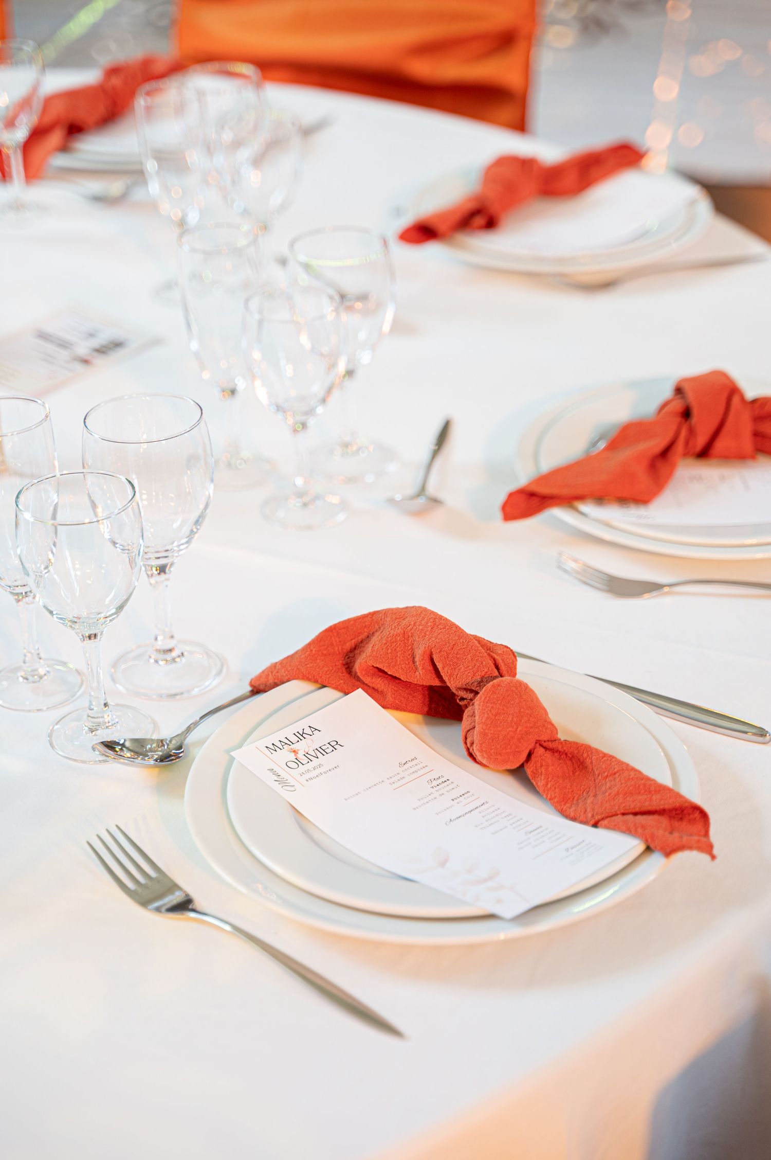 Formal wedding reception table with white linens, orange knotted napkins, menus, and clear wine glasses.