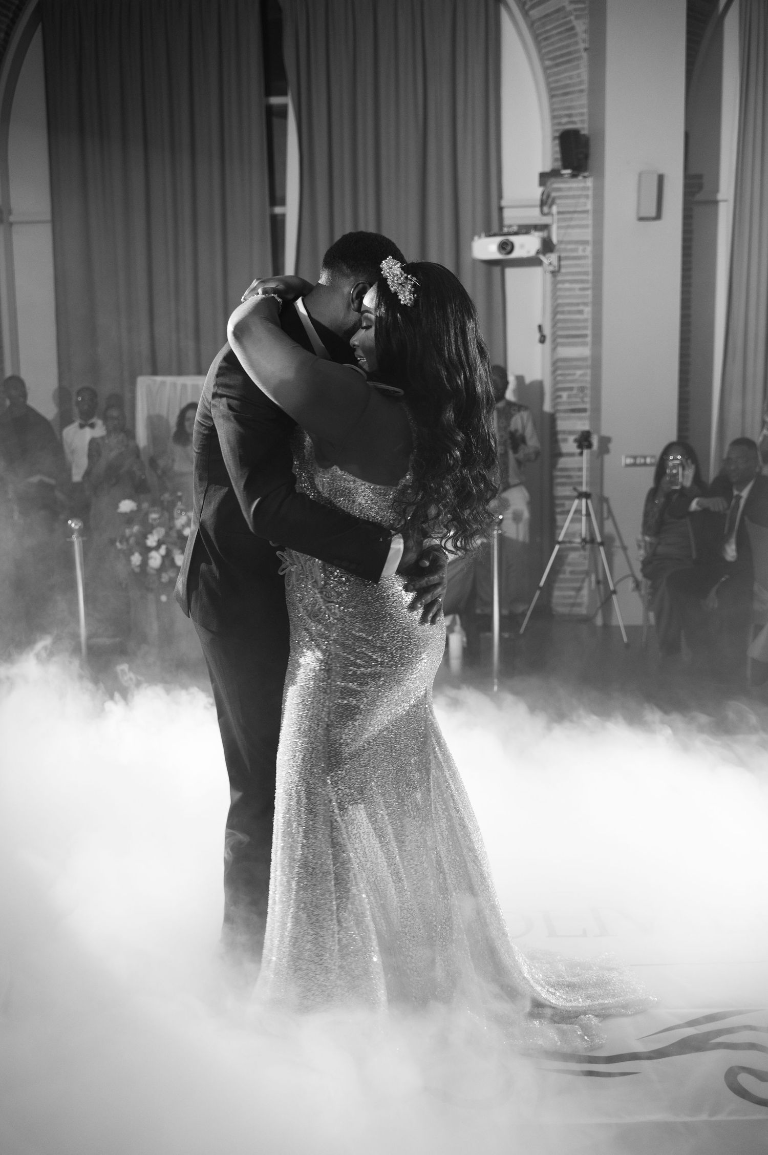 Black and white photo of newlyweds sharing romantic first dance kiss enveloped in wedding fog.