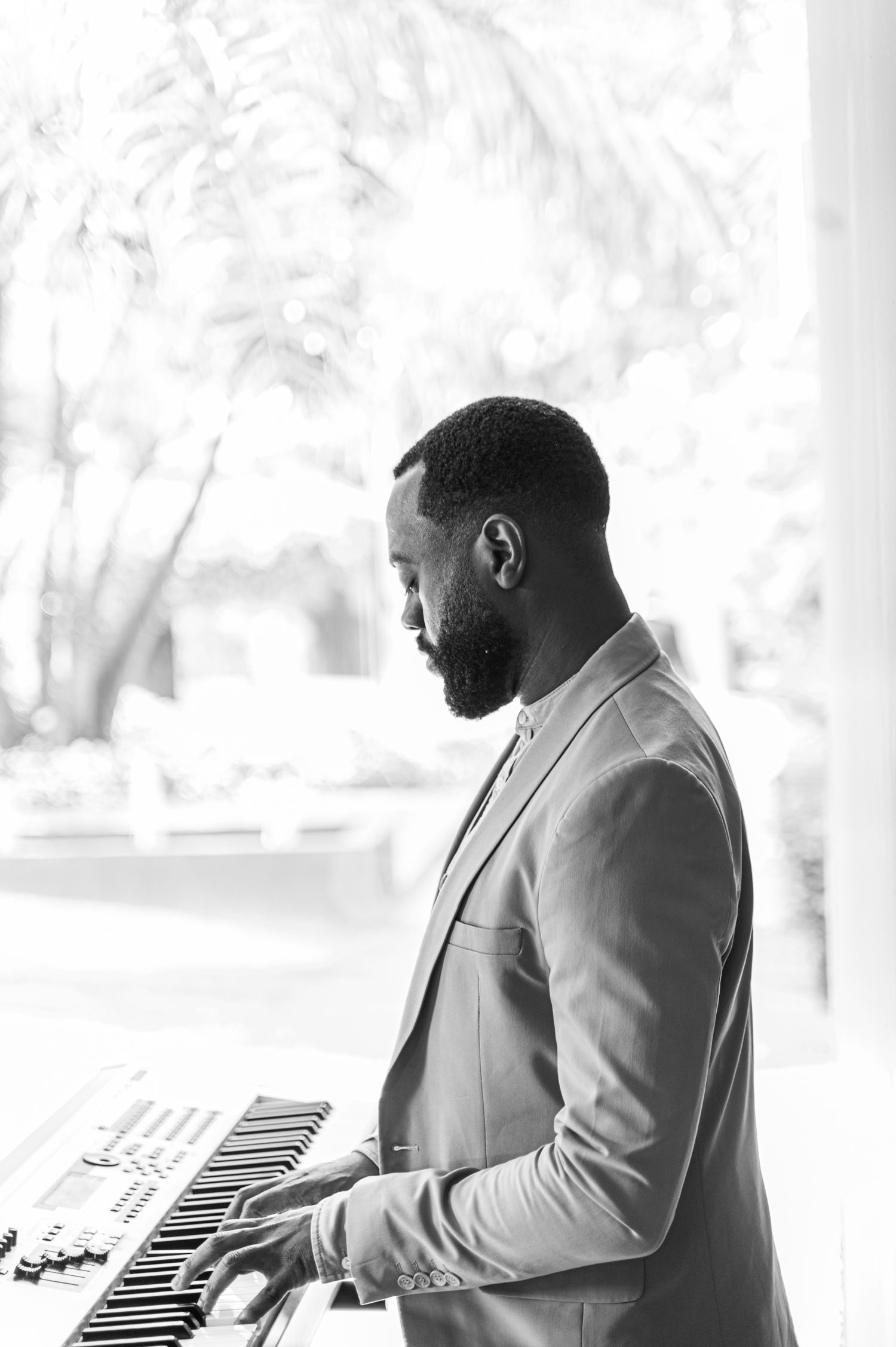 Black and white portrait of a bearded man in a suit playing a keyboard at a wedding.