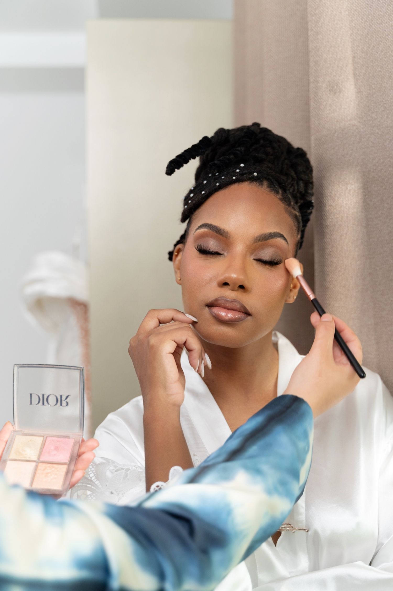 Makeup artist applying Dior blush to a smiling bride in a white robe.