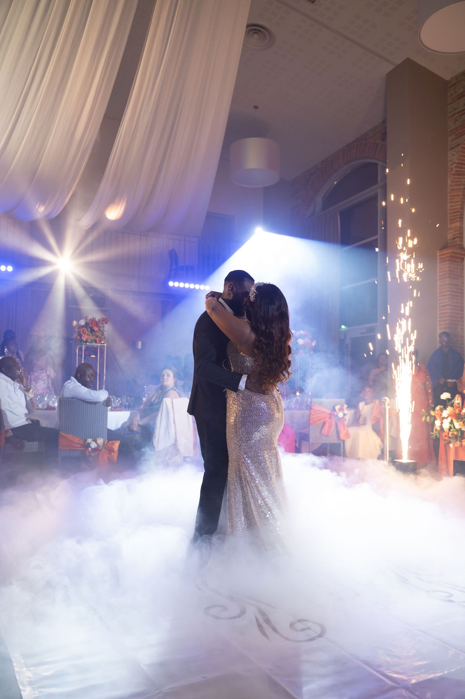 Couple dances romantically on fog-filled dance floor with dramatic lighting and fireworks at wedding.