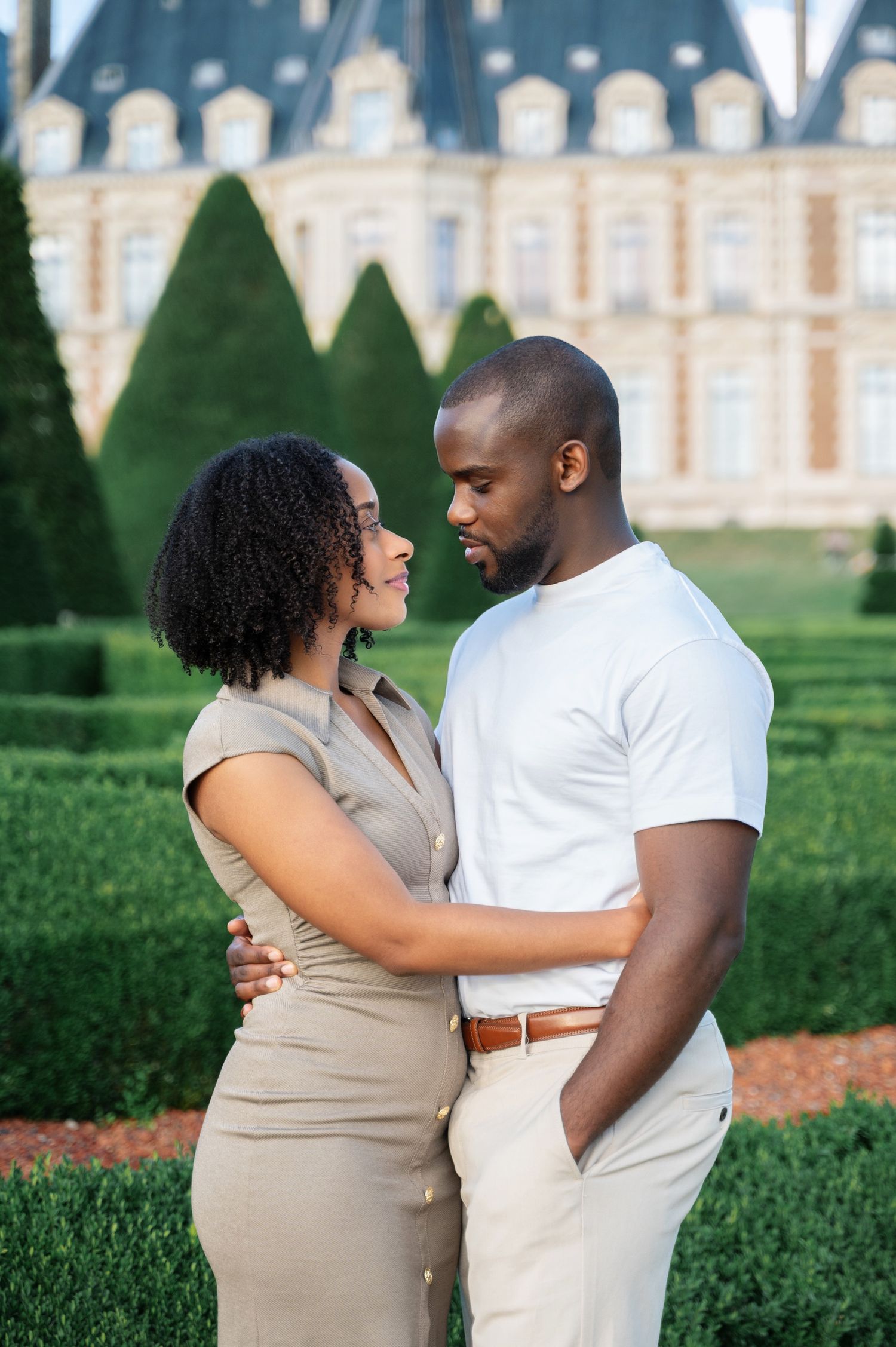 Couple embracing and gazing at each other with French chateau garden backdrop.