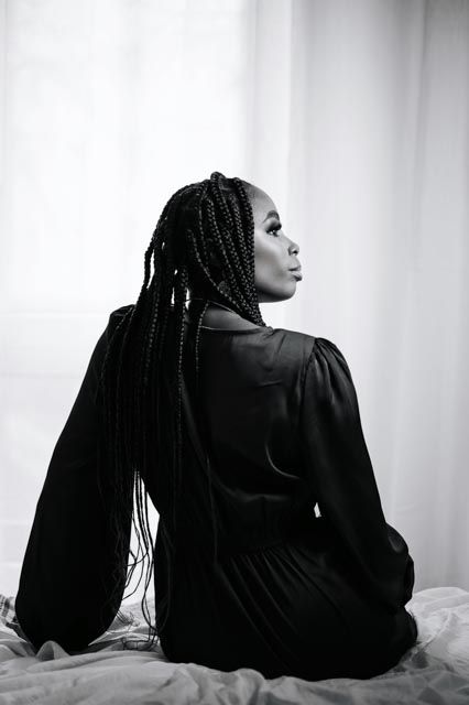 Black and white portrait of woman with long box braids in black satin dress seated gracefully.