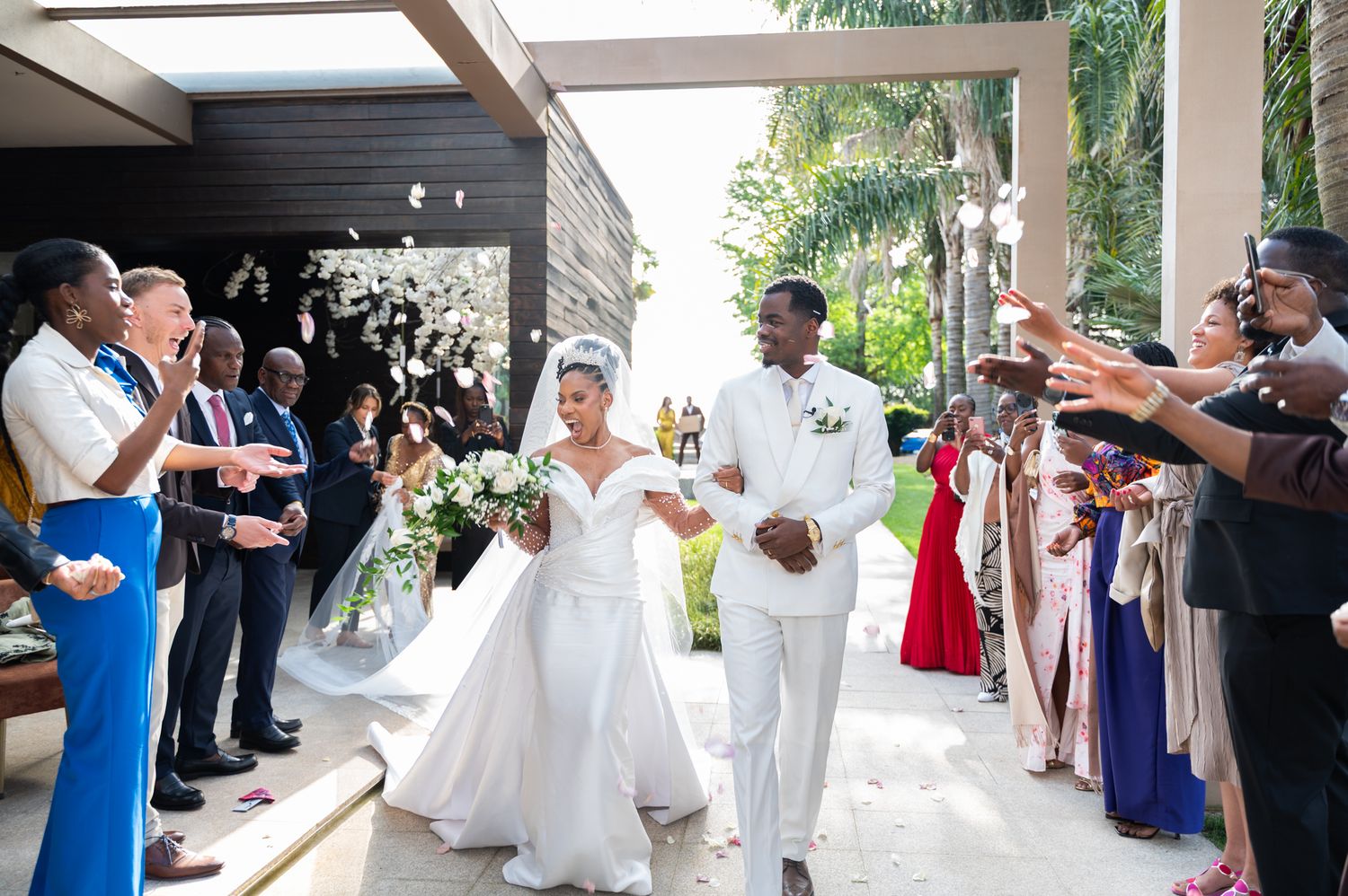 Newlyweds walking through celebratory send-off with guests cheering at wedding.
