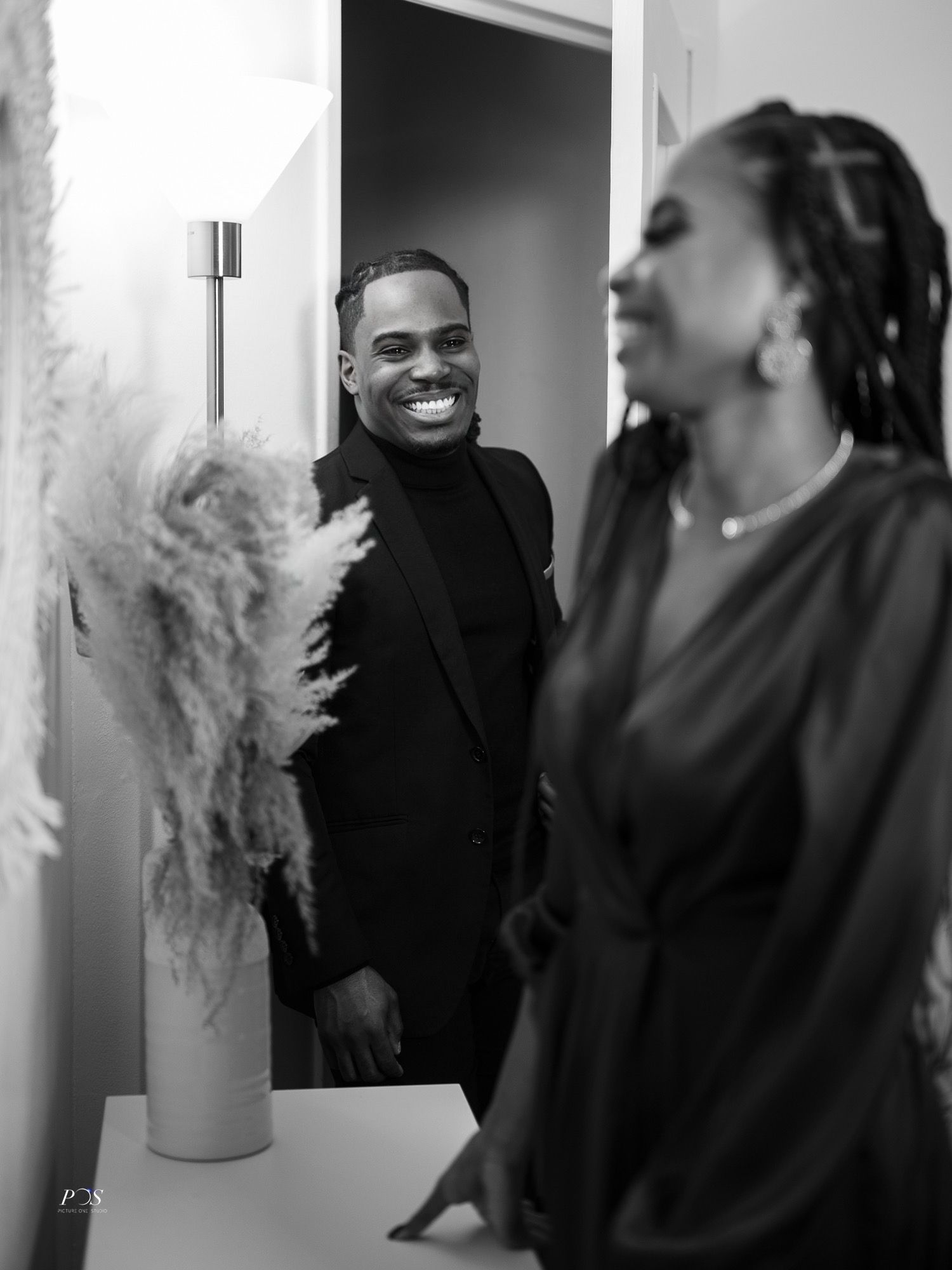Smiling man in black suit laughs with woman in black dress in black and white interior photo.