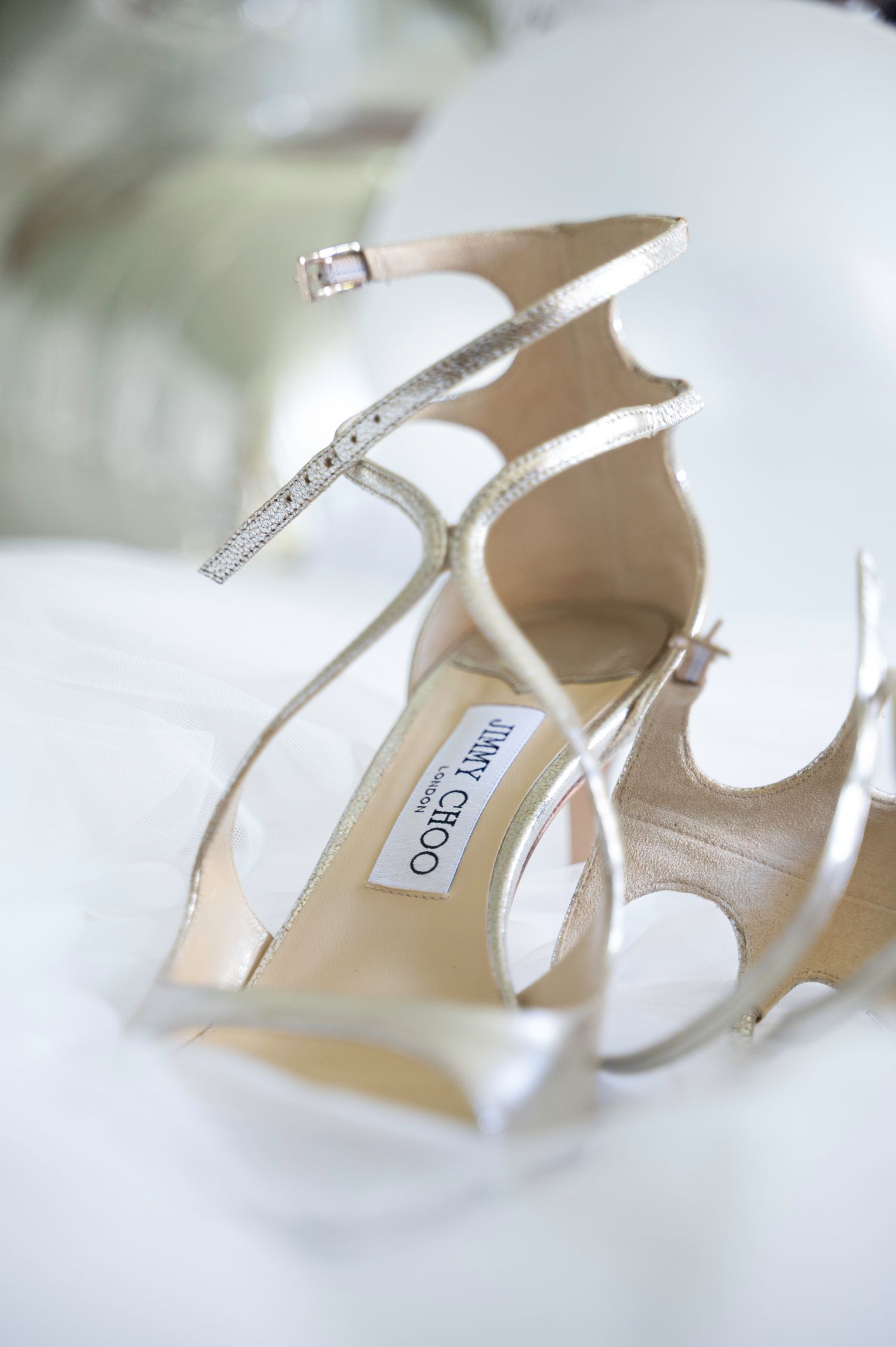 Jimmy Choo silver strappy high heel sandals resting on white bridal veil fabric.