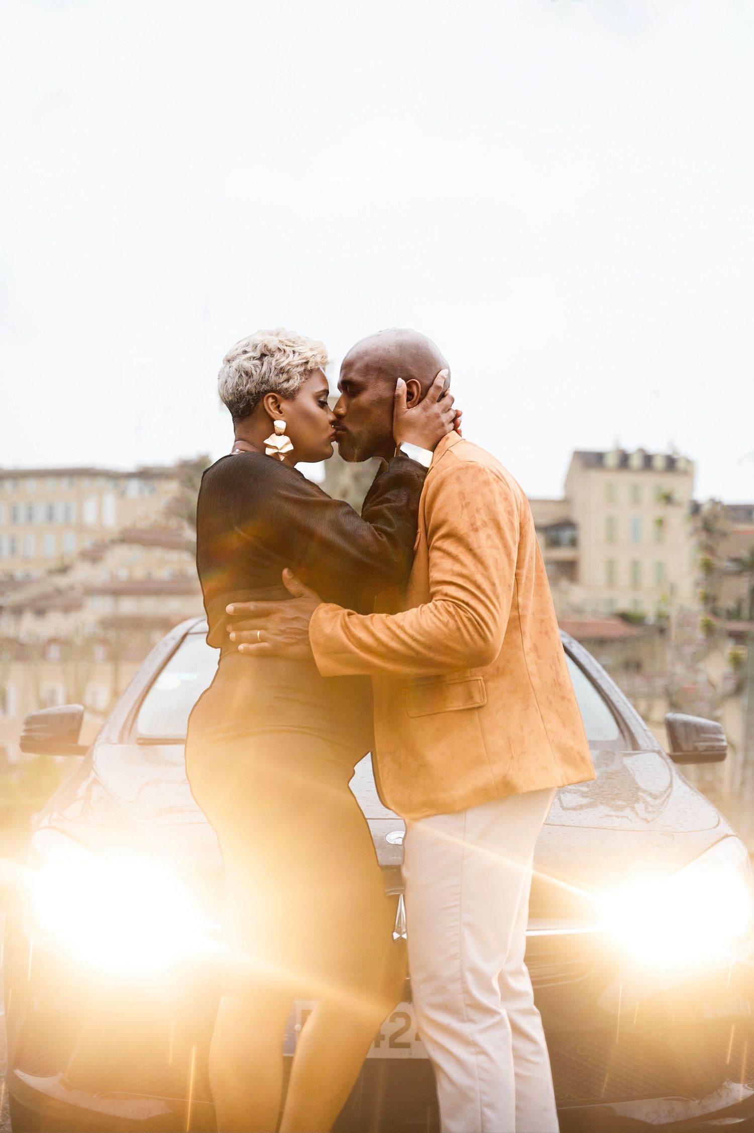 Black couple kissing passionately in front of a car with warm golden backlight.