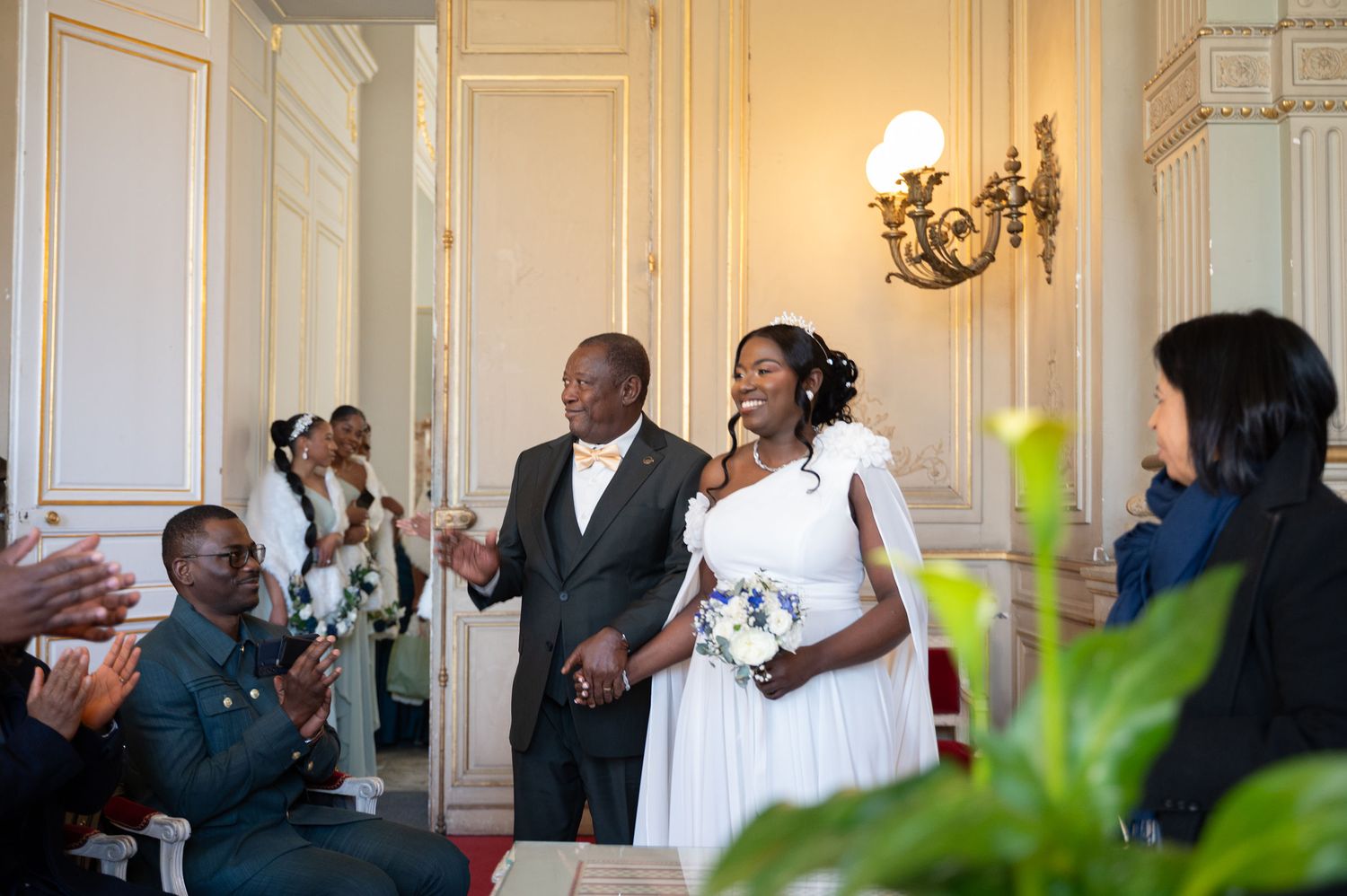 Bride walks down aisle with escort at elegant wedding ceremony in classic white hall.